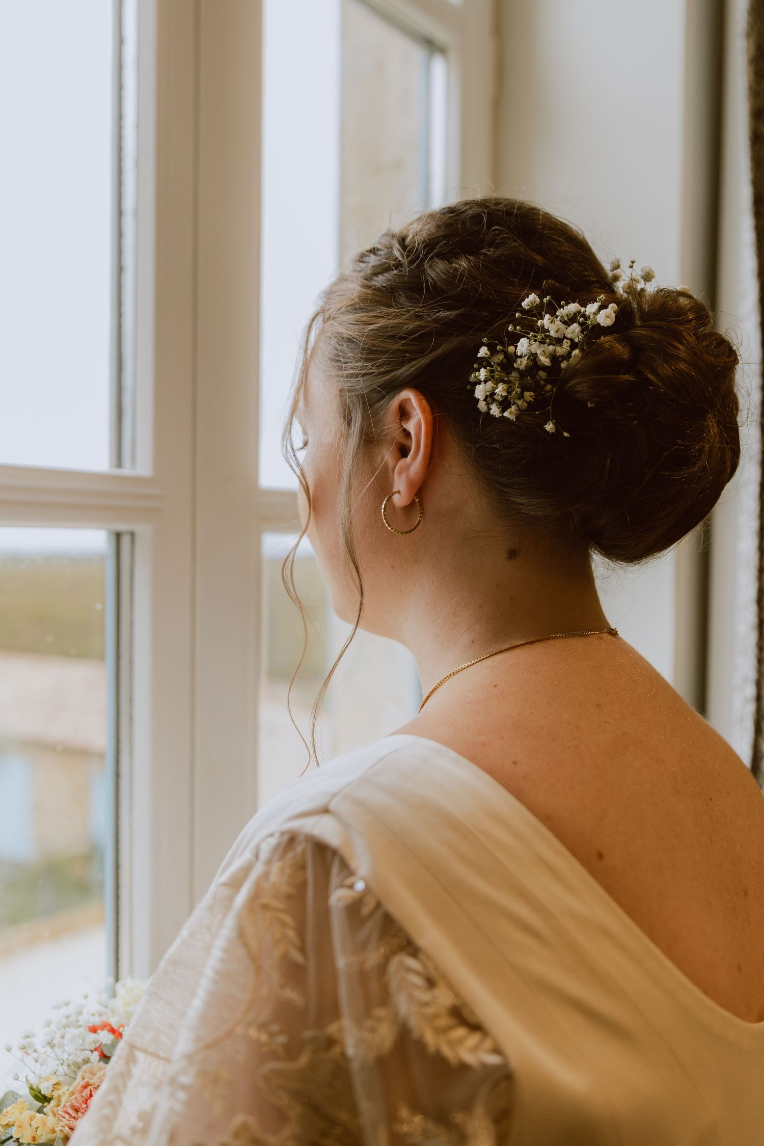 Une mariée avec une belle coiffure regarde en dehors de la fenêtre.