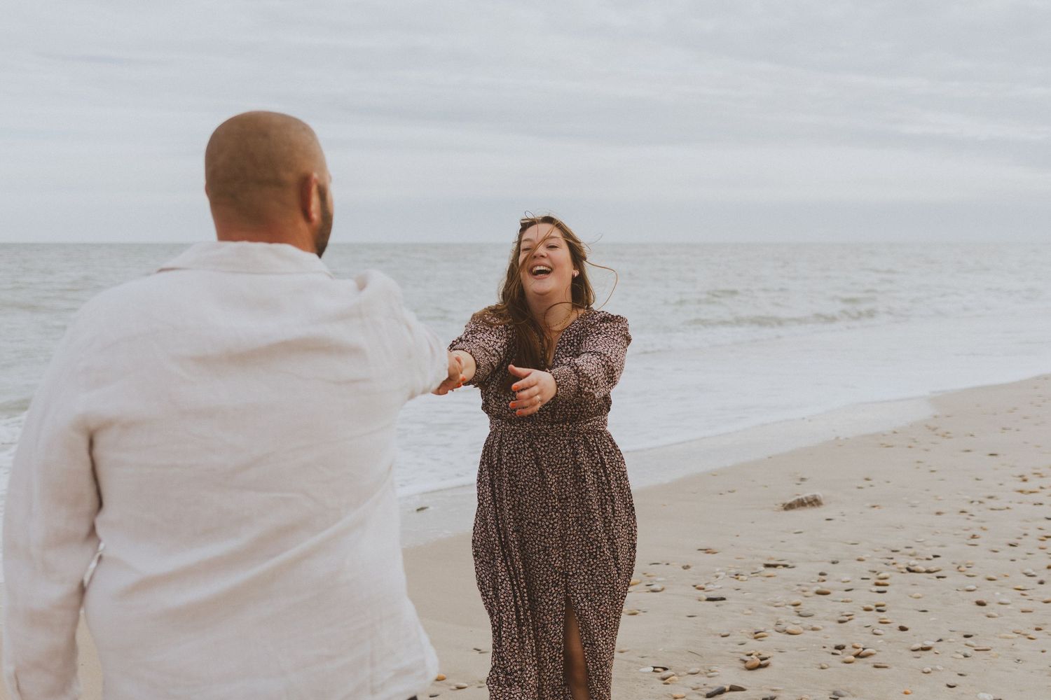 Un couple danse ensemble lors d'une séance photo engagement, au bord de la mer aux Aresquiers, lors d'une journée grisâtre