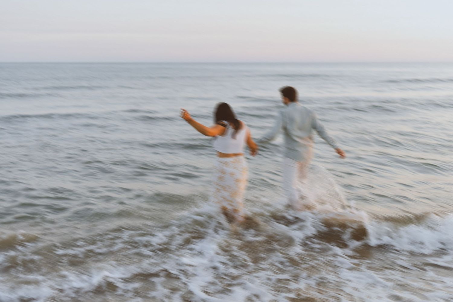Un couple court main dans la main vers la mer, pendant un joli coucher de soleil.