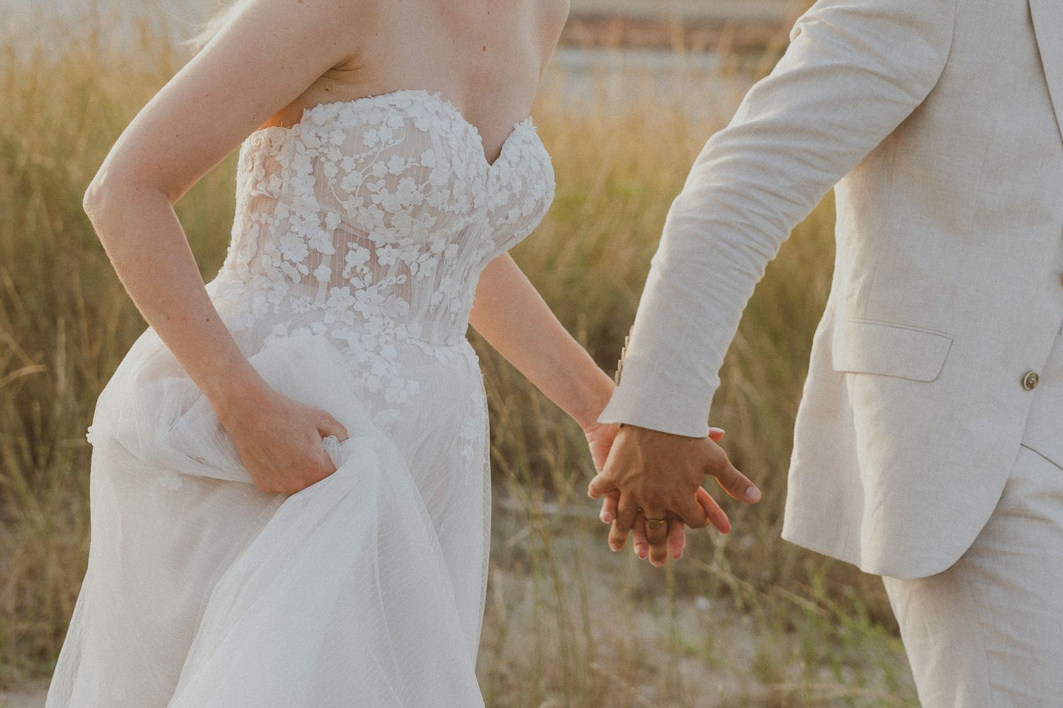 Un couple de mariés se tient la main dans un champ pendant la golden hour. Photo par Alice Enrico, photographe mariage à Montpellier.