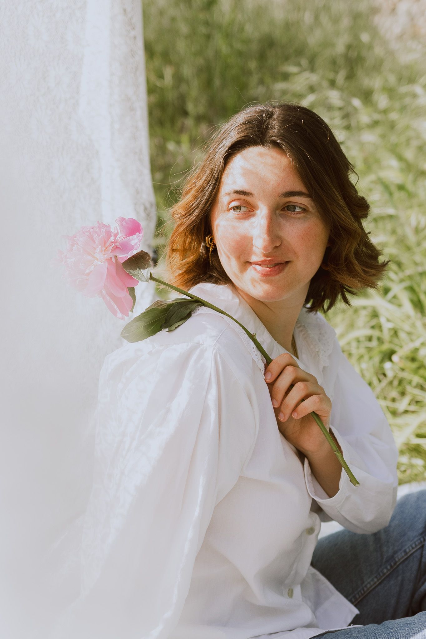 Une jeune fille pose pour une séance photo spéciale confiance en soi, en tenant une fleur rose dans un décor printanier.