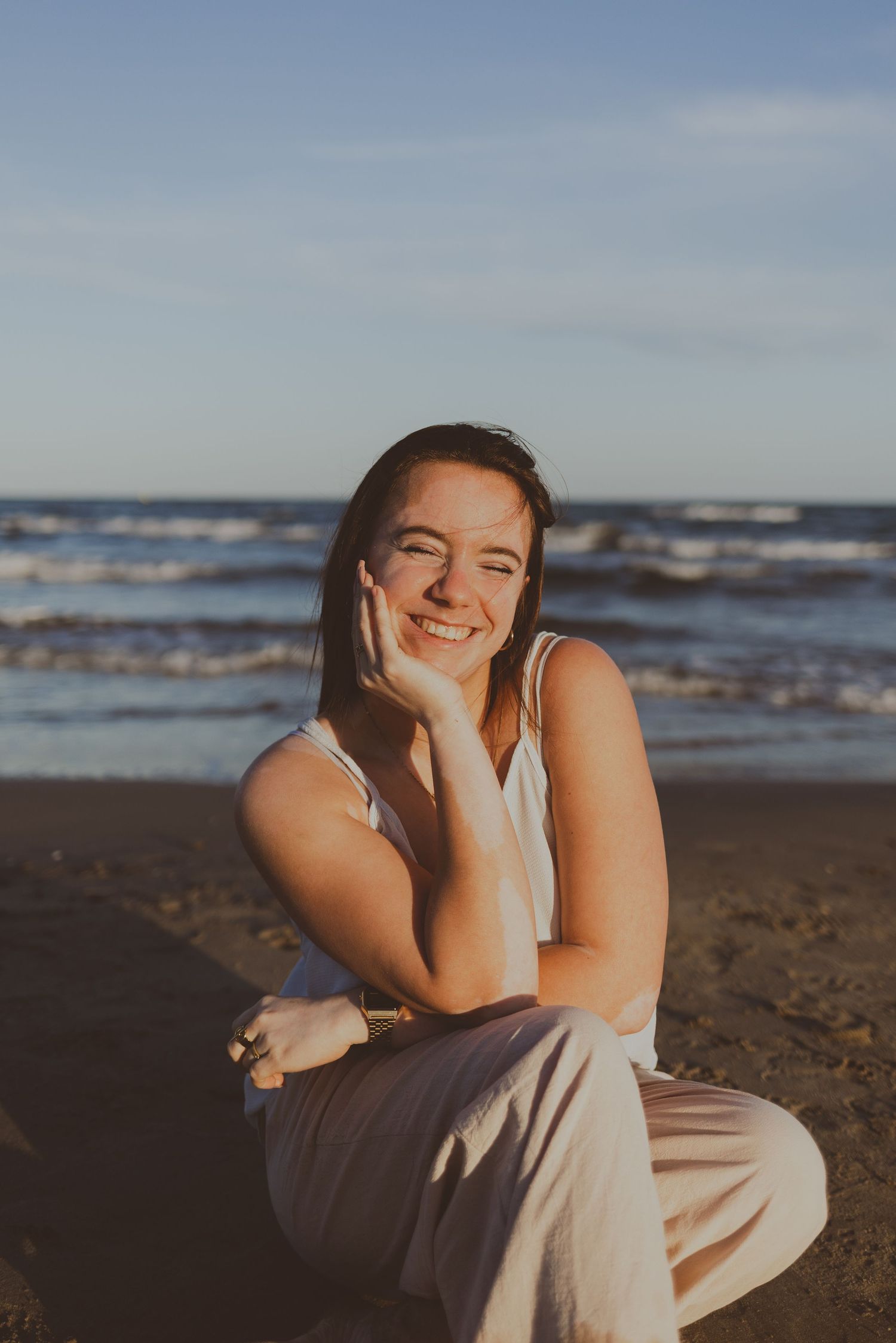 Une jeune fille souriante pose au bord de la mer pendant une séance photo au coucher de soleil.