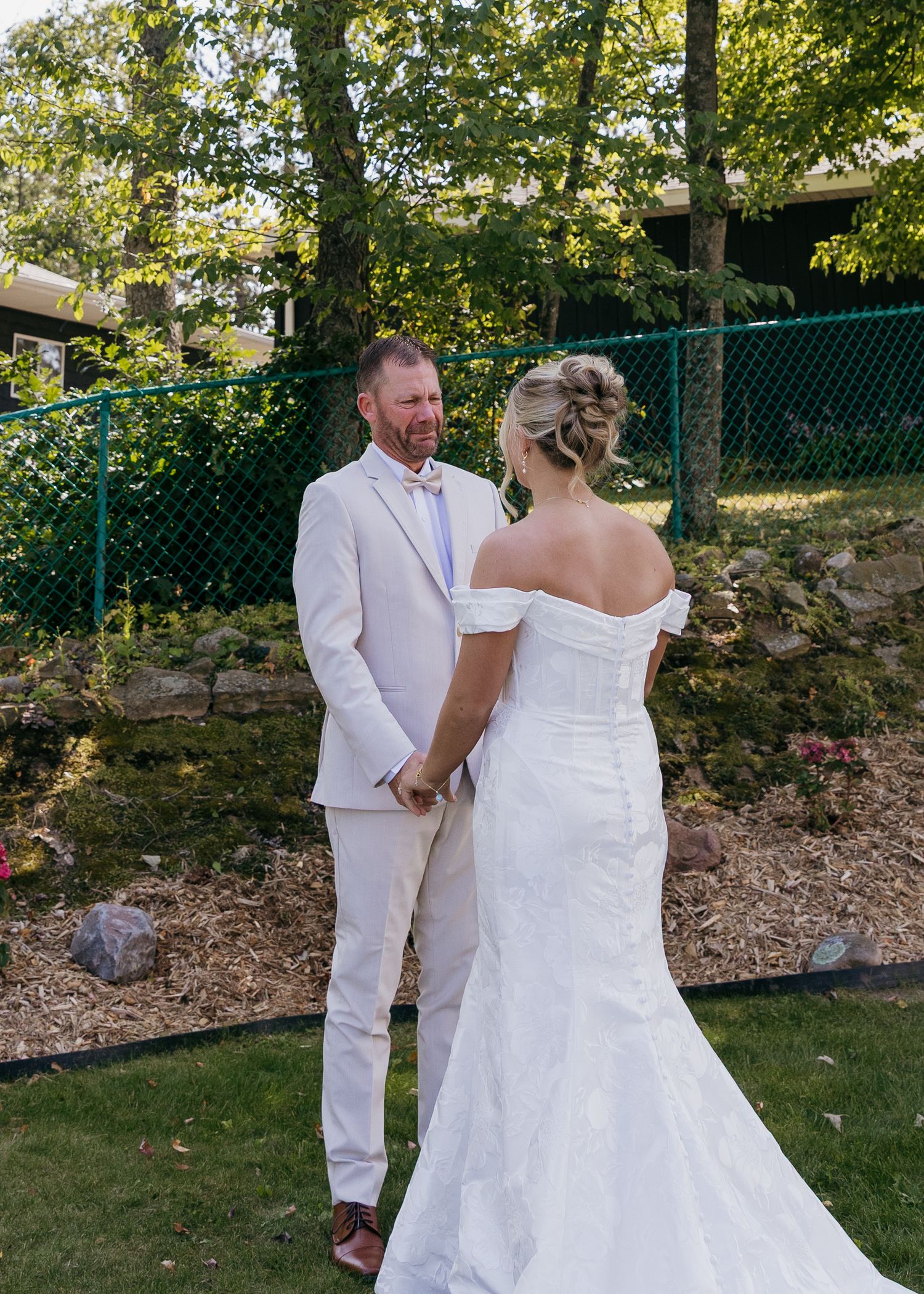 Couple in white wedding attire standing together outdoors during ceremony.