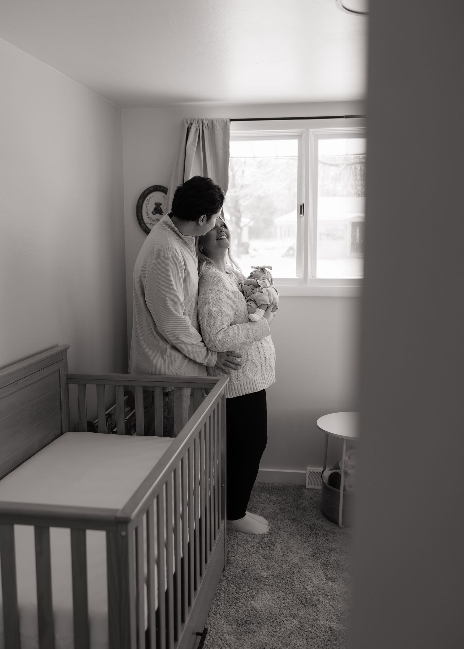 A tender black and white nursery moment with a crib and window.
