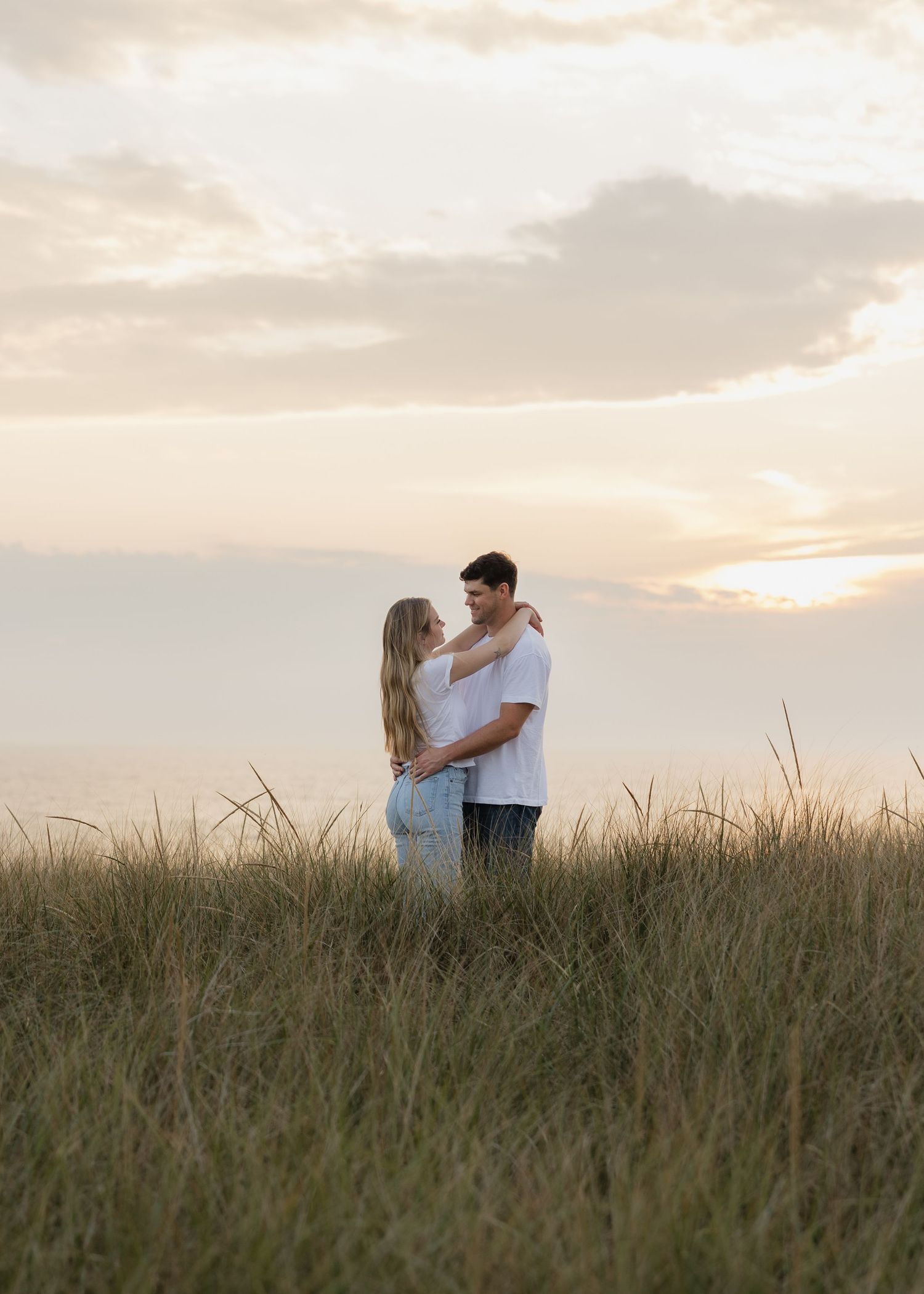 Silhouetted couple standing in tall grass field during golden sunset.