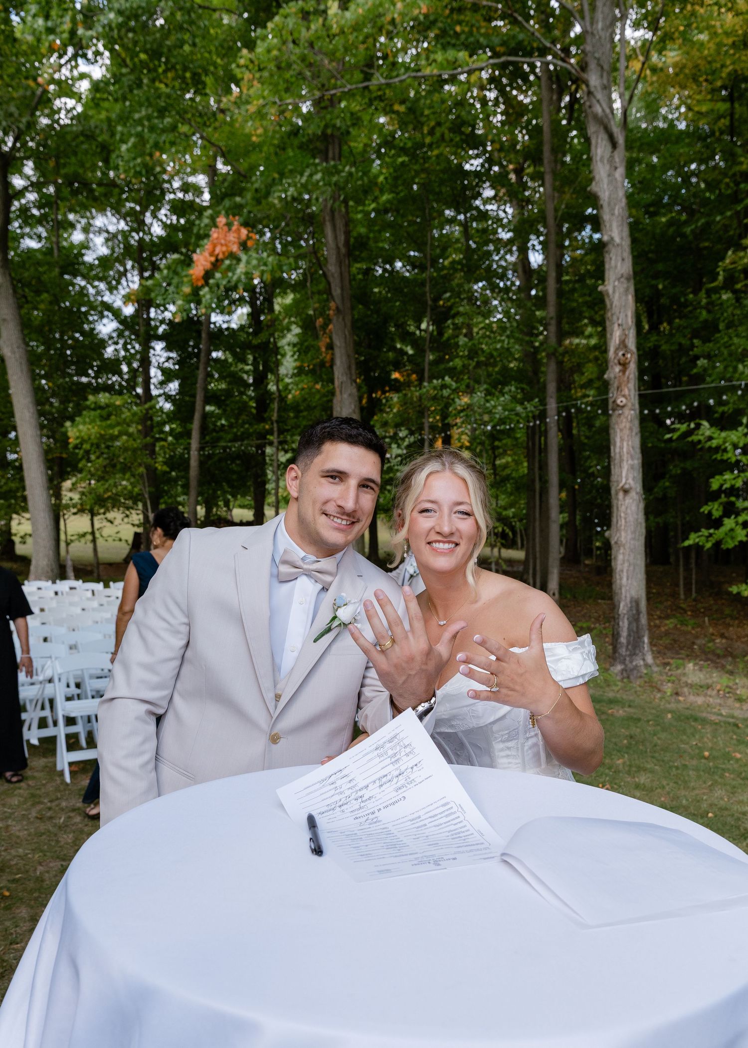 Wedding couple poses at signing table during outdoor celebration.