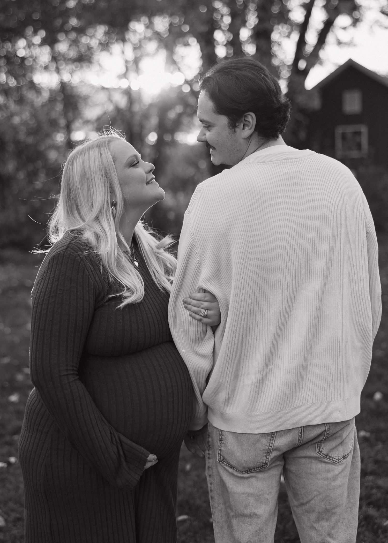 A black and white intimate portrait of an expecting couple sharing a tender moment outdoors.