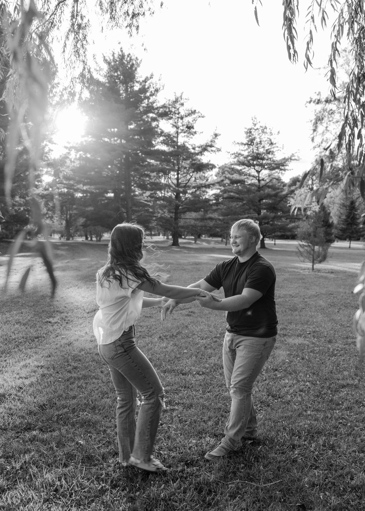 Dancing couple in black and white silhouette under willow trees at sunset.