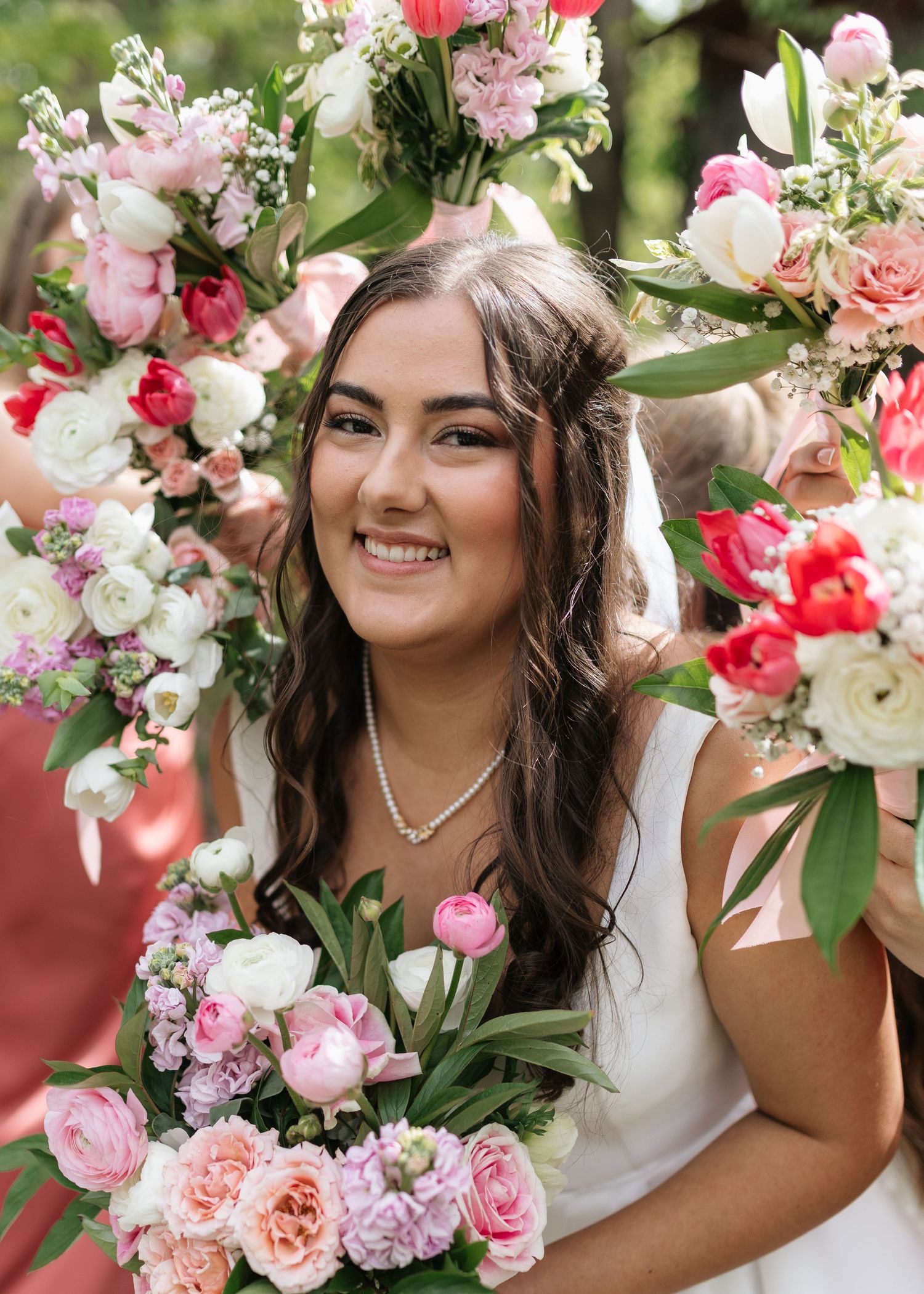Smiling bride in white dress surrounded by pink and white floral bouquets and flower arch on her wedding day.