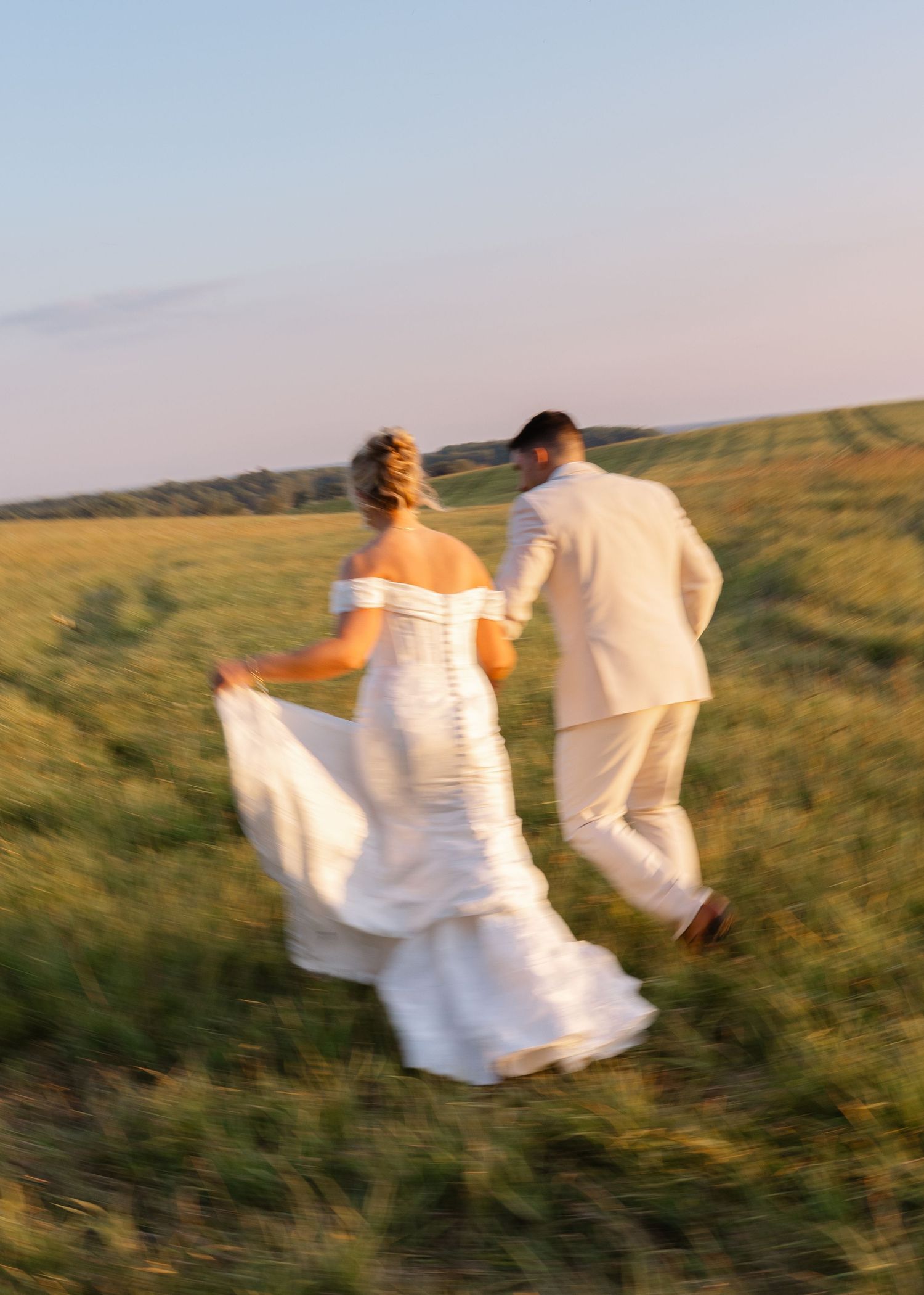 Motion shots of couple running through field in white formal wear at sunset.
