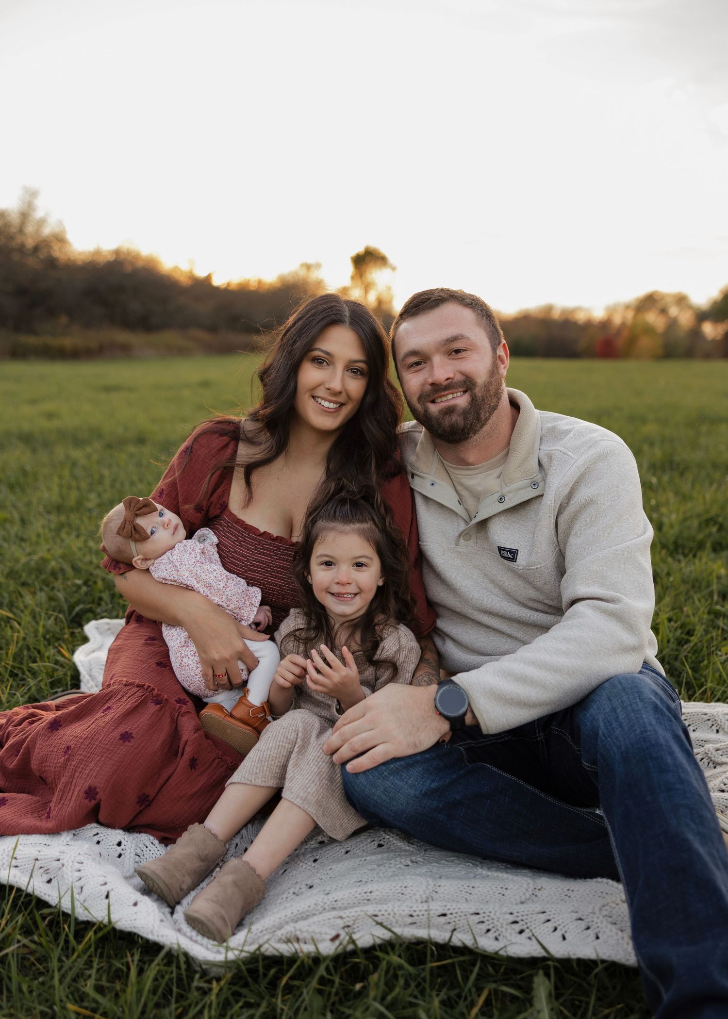 Family portrait session on blanket in field during sunset with warm lighting.