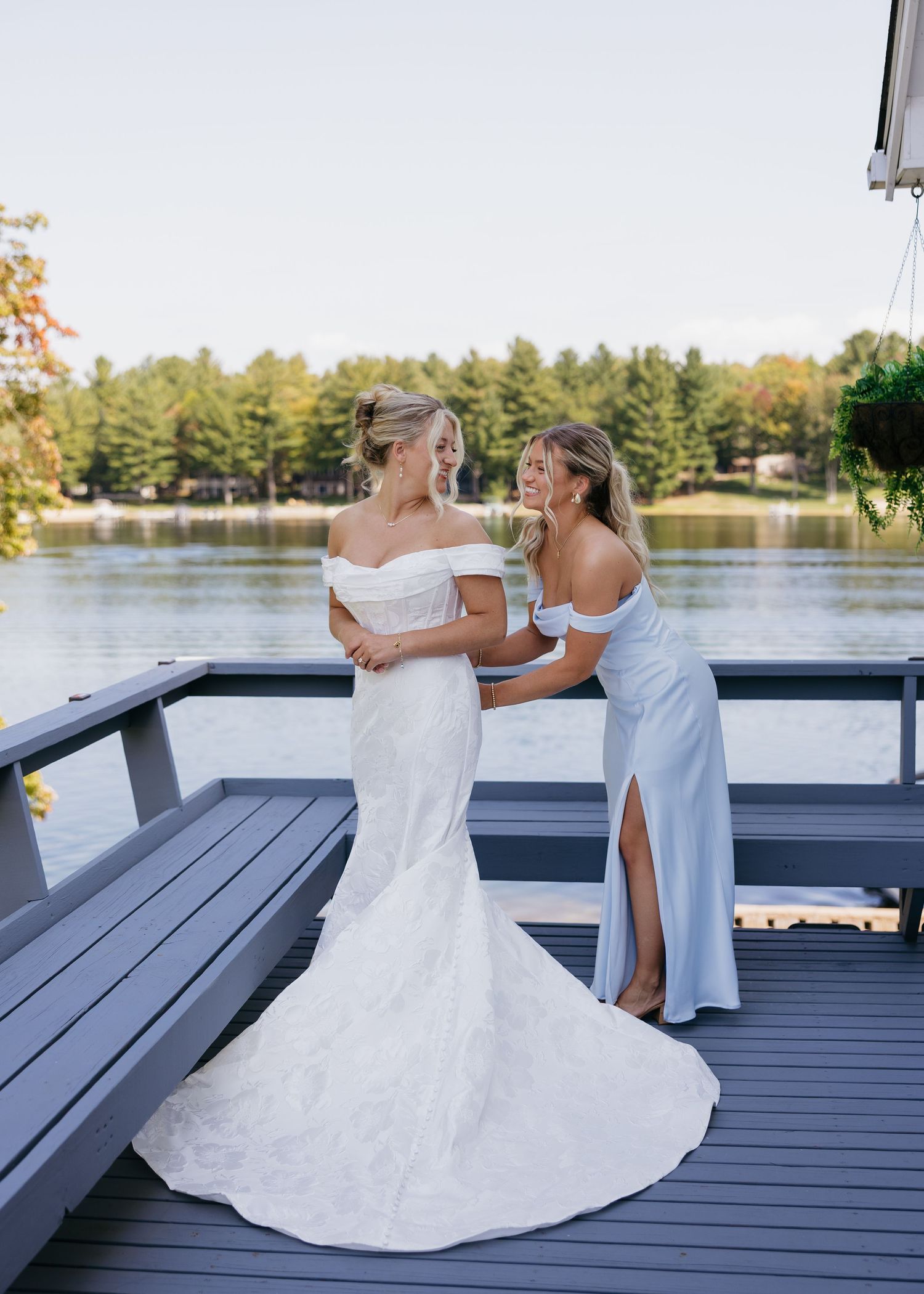 Two people in white dresses sharing a moment on a lakeside deck.
