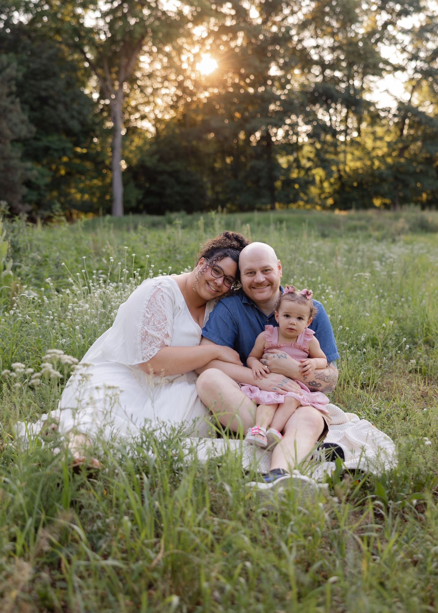 Family sitting together in wildflower meadow during golden hour sunset.