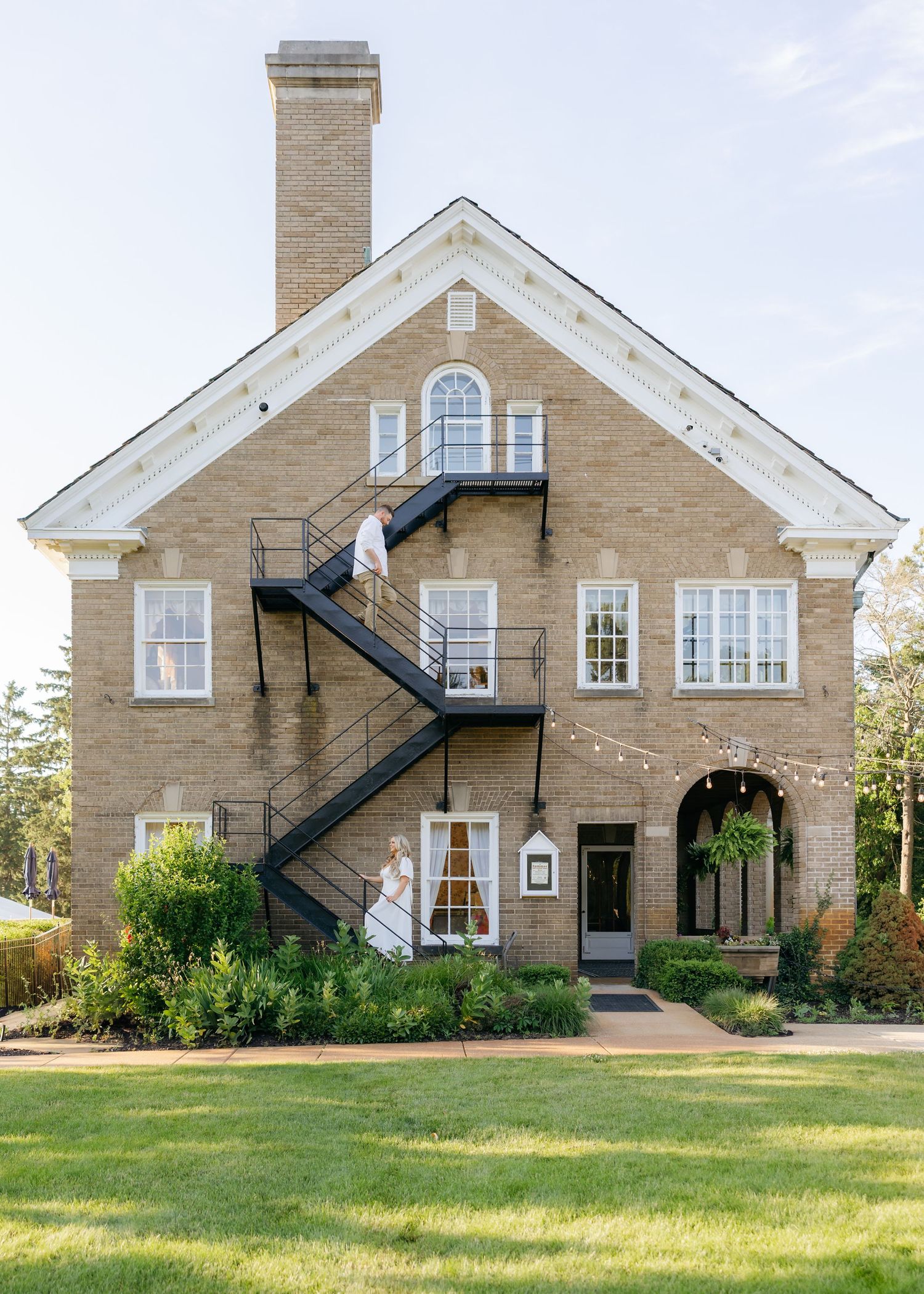 Exterior views of a beautiful stone mansion with white trim and arched windows on a sunny day.