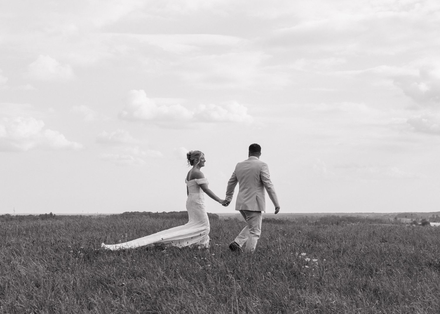 Couple walking together through a serene meadow at sunset in black and white.