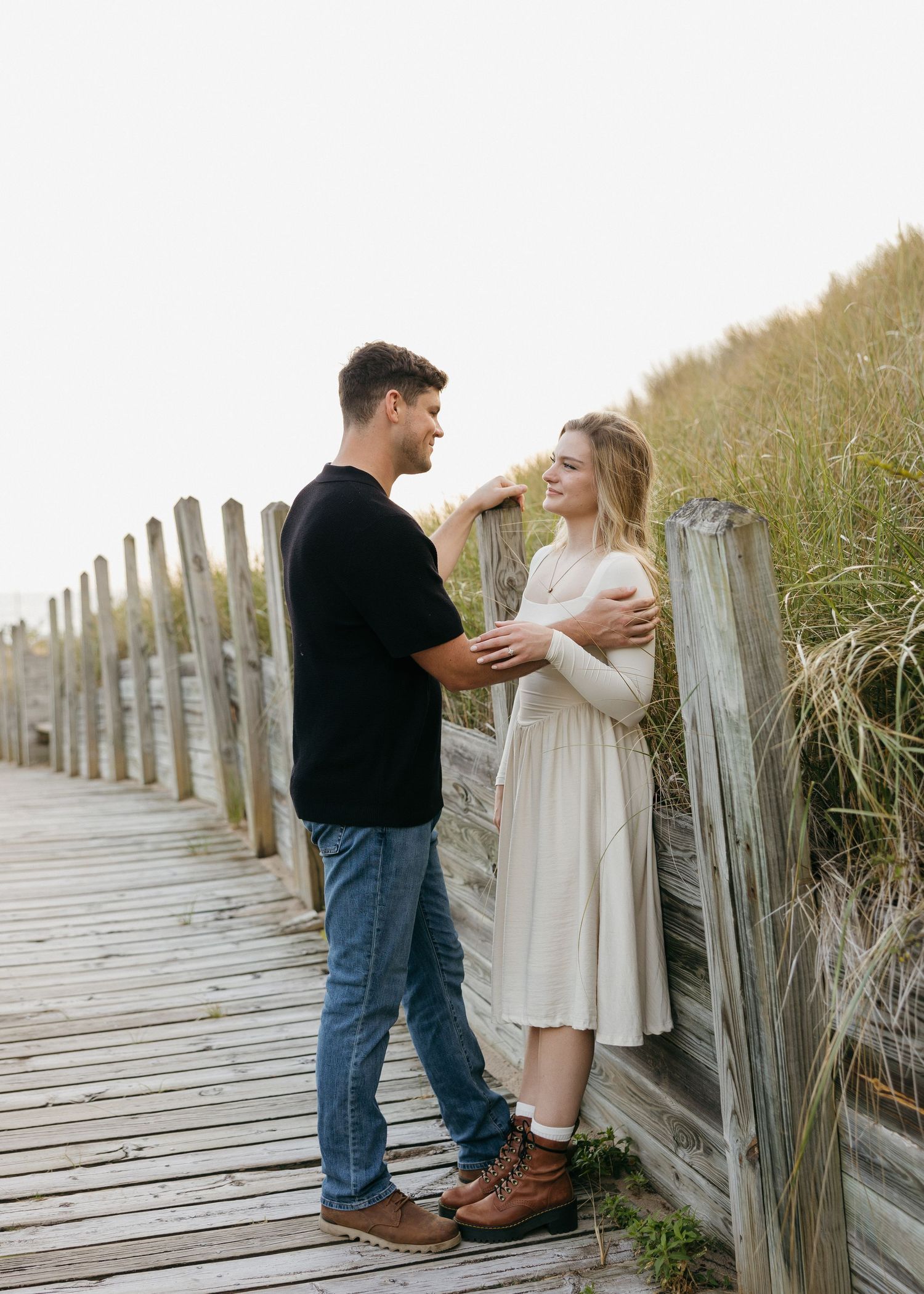 Couple embracing on a rustic wooden boardwalk near coastal dunes.
