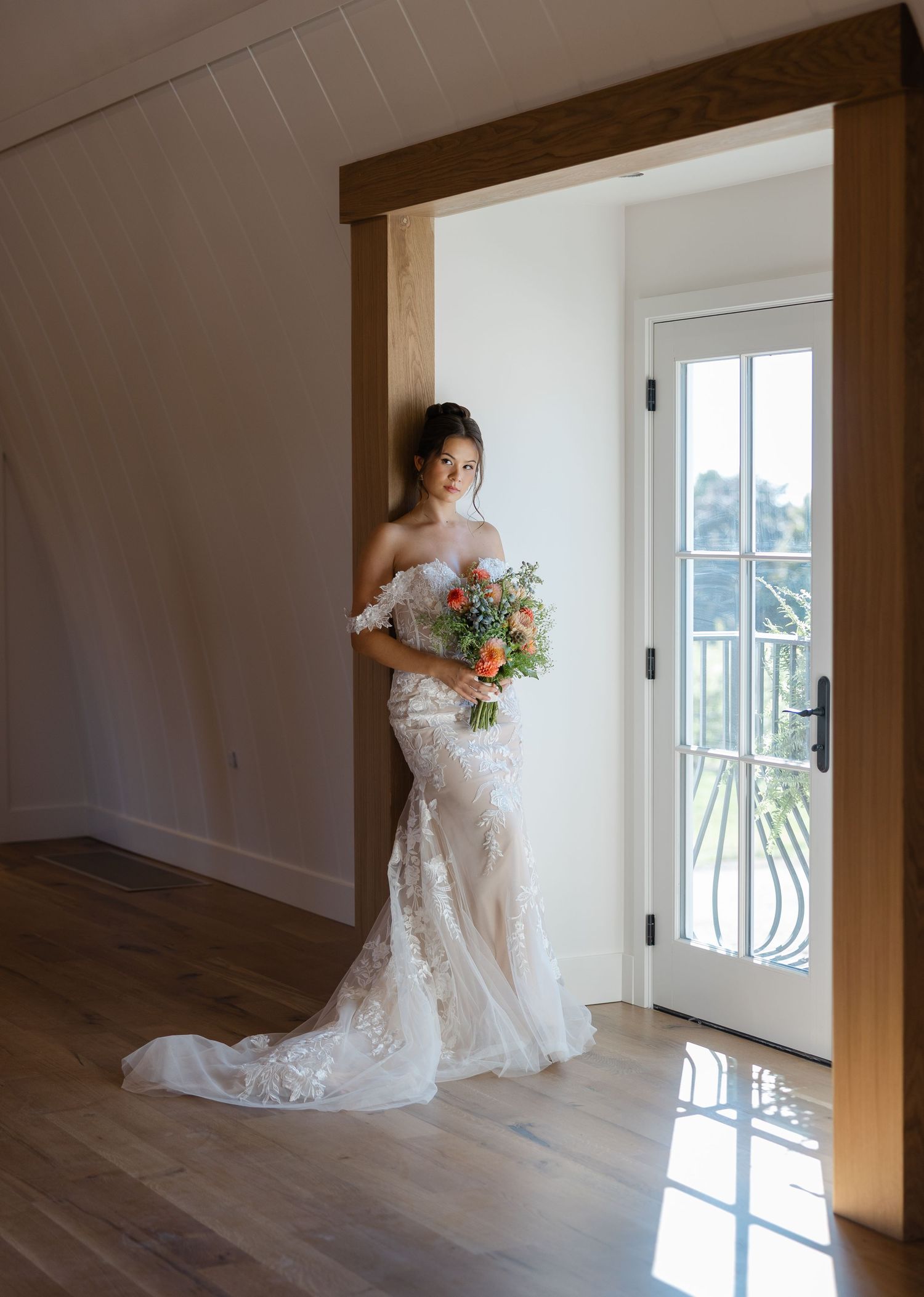 Elegant bridal portrait in lace gown with colorful bouquet by doorway.