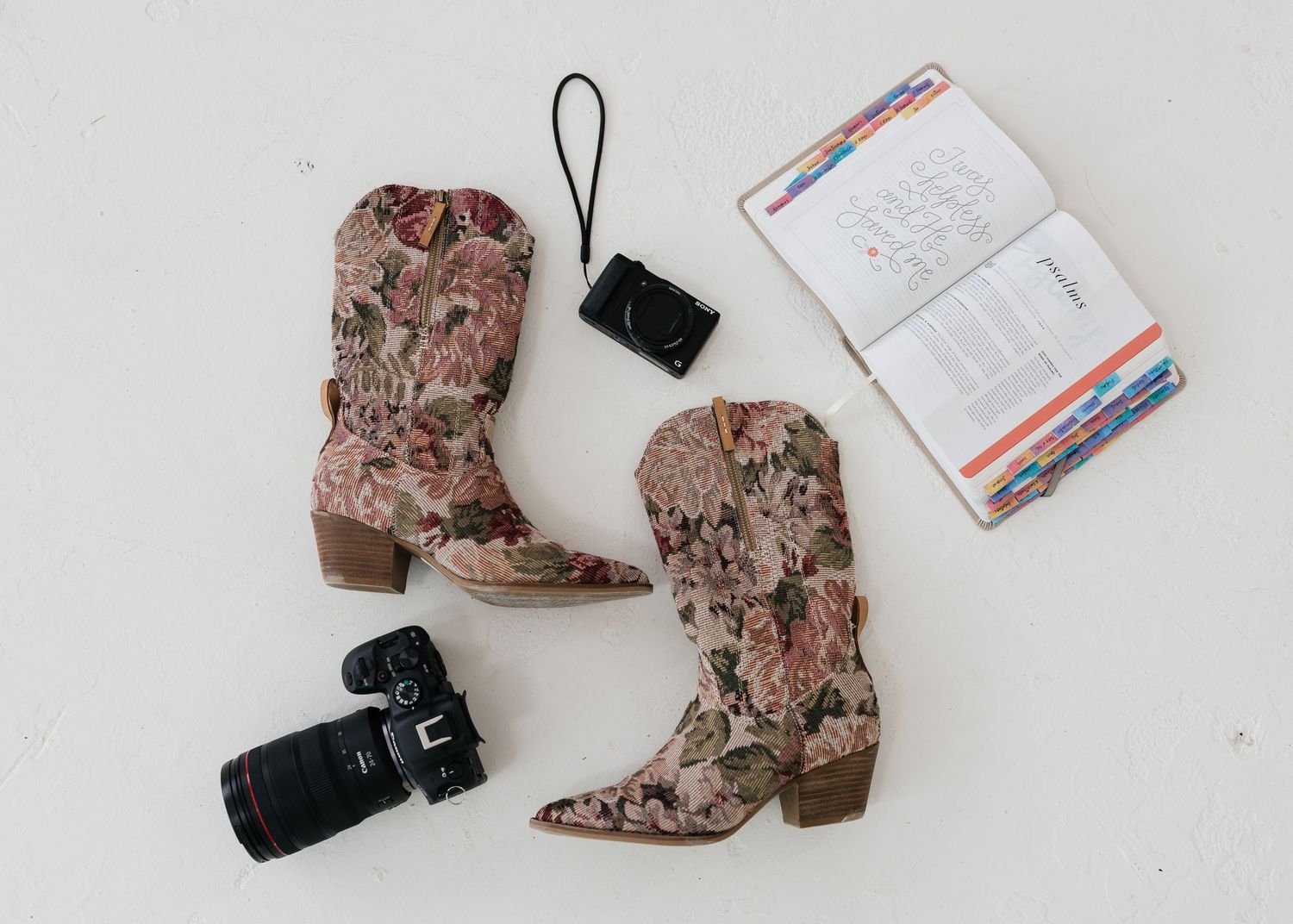 Flatlay of photography equipment and snakeskin boots on white background.