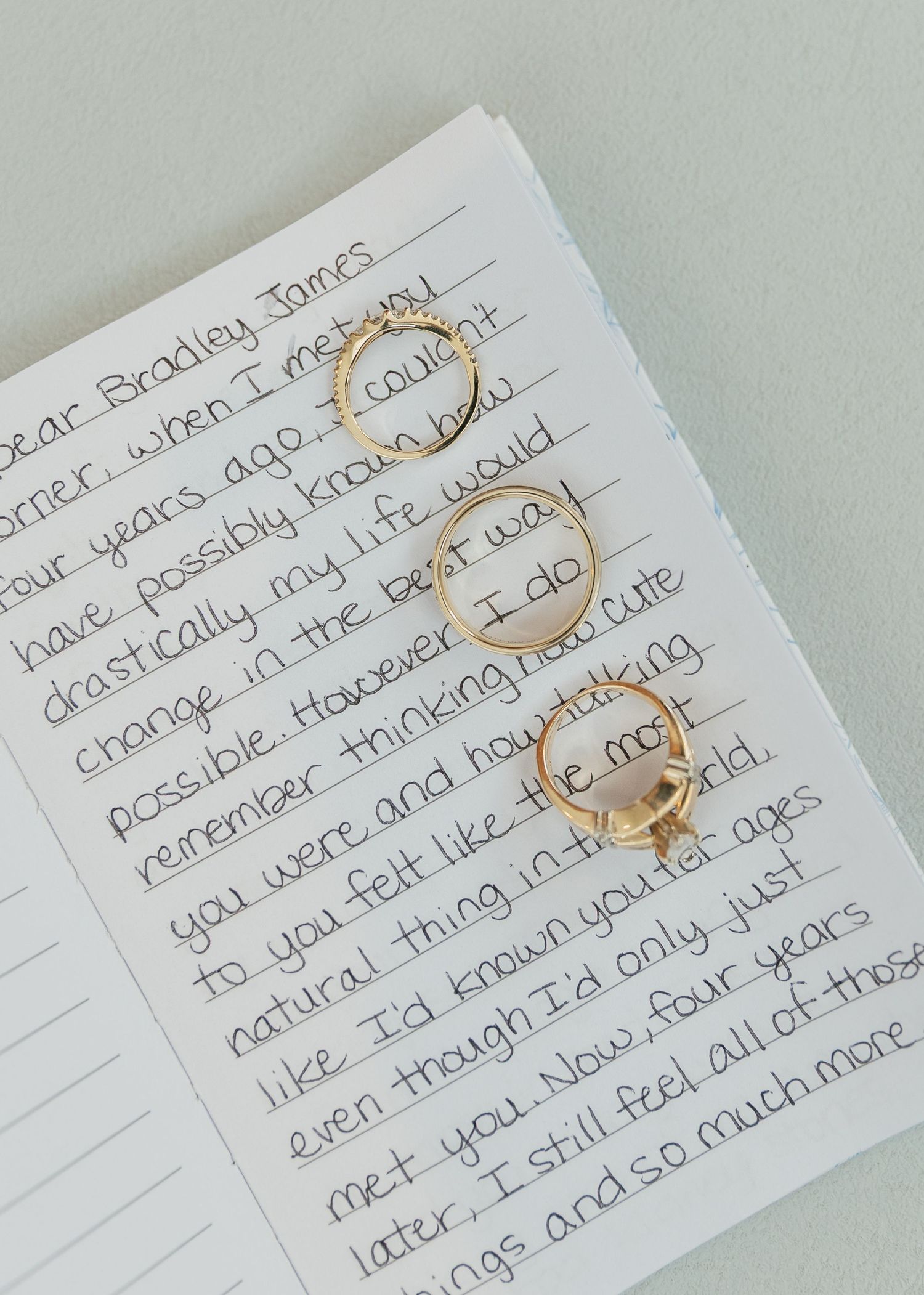 Gold rings resting on a handwritten love letter addressed to Bradley James on a white notepad with mint background.