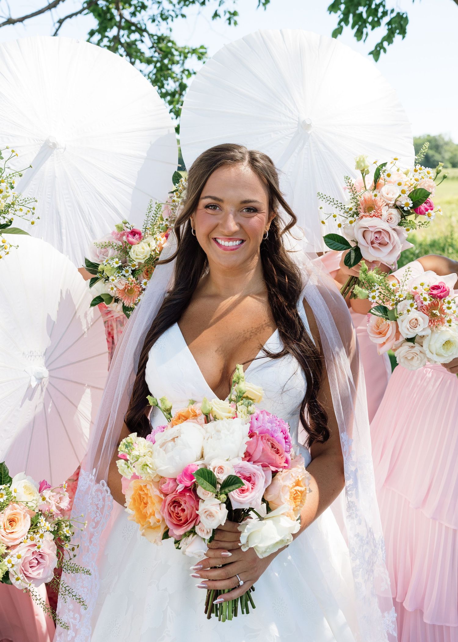 Smiling bride in white V-neck gown holds colorful bouquet with white paper fan decorations behind her.