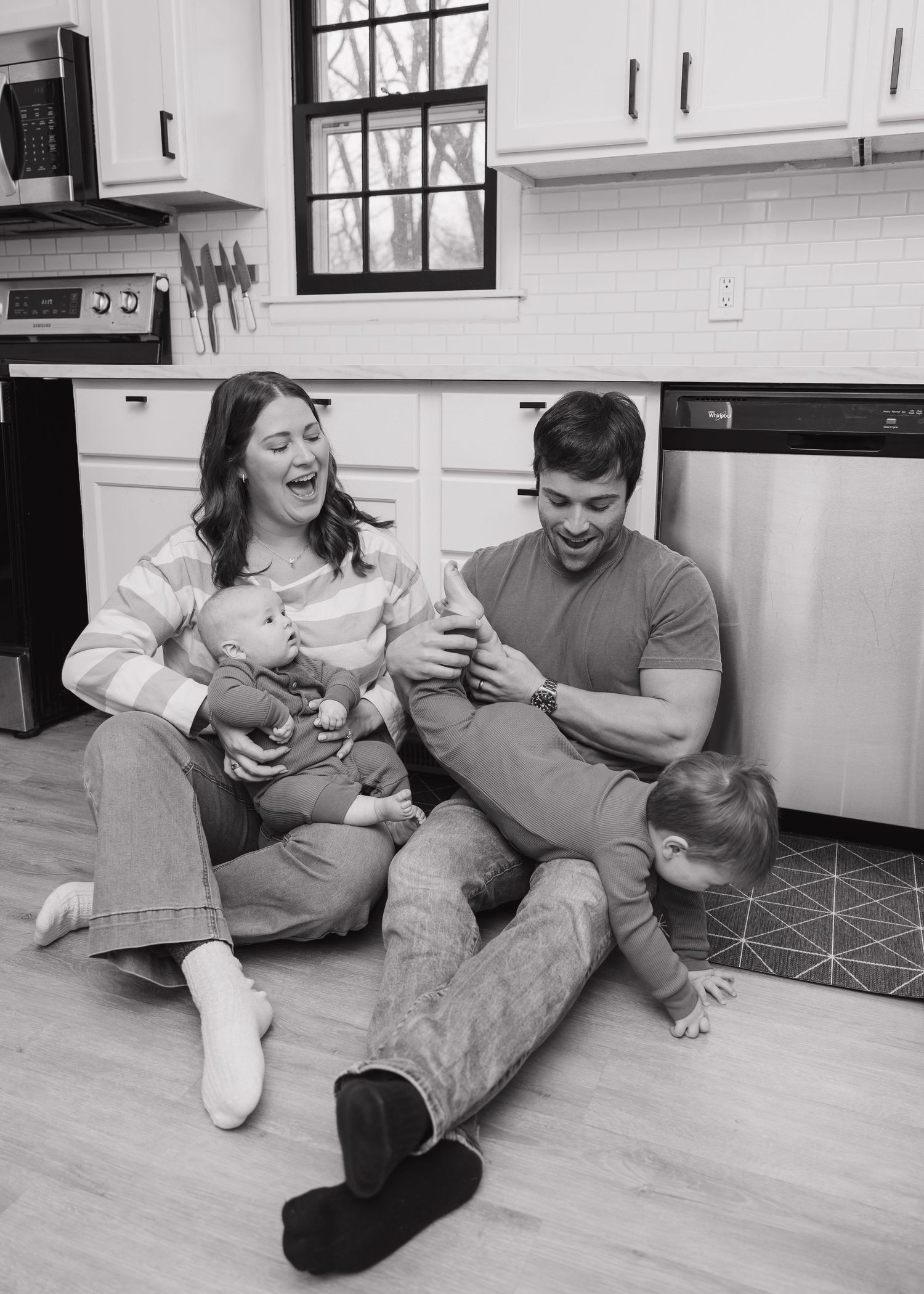A family sits together on their kitchen floor sharing a playful moment.