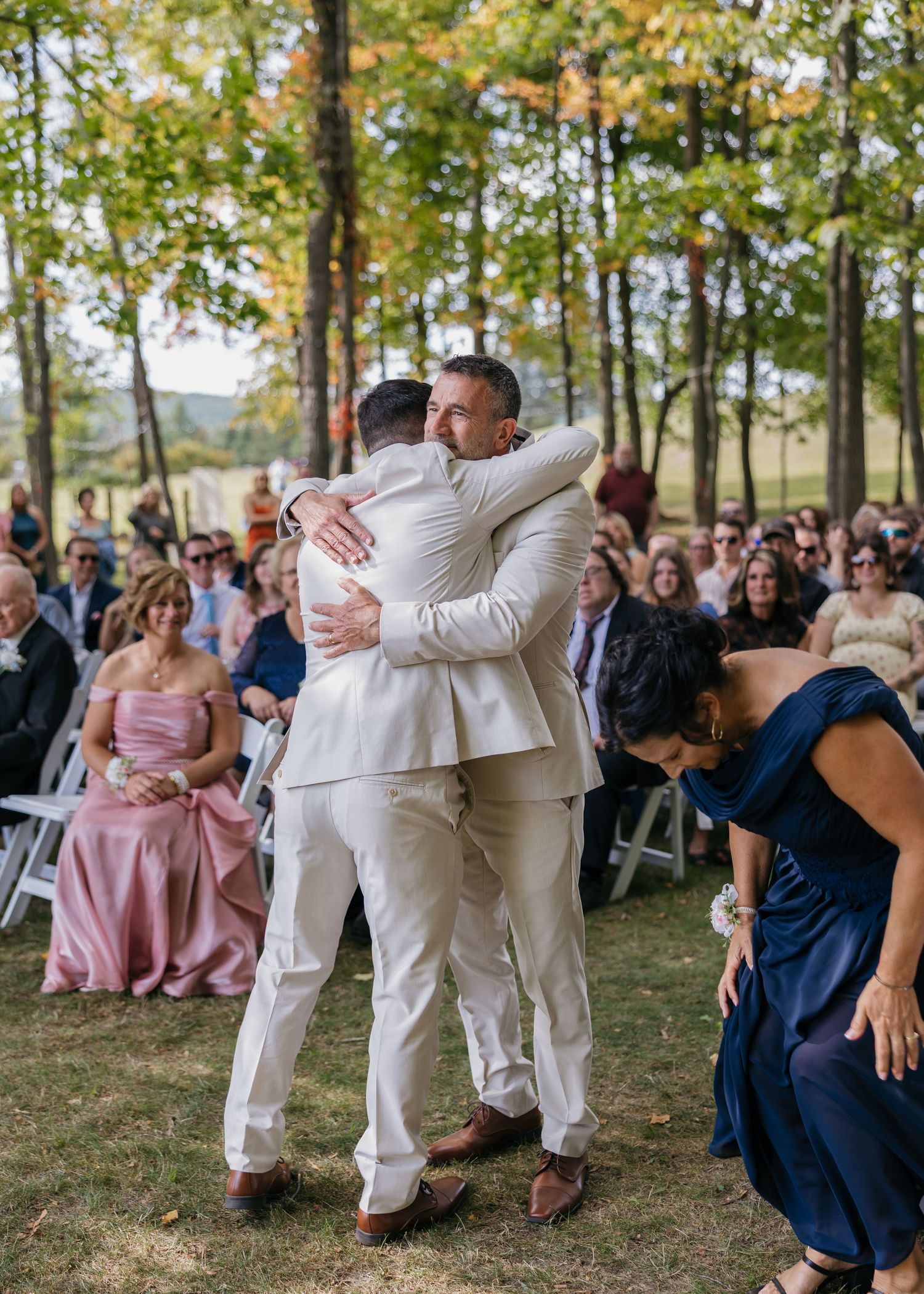 Wedding guests and party members dance outdoors under trees during a celebration.