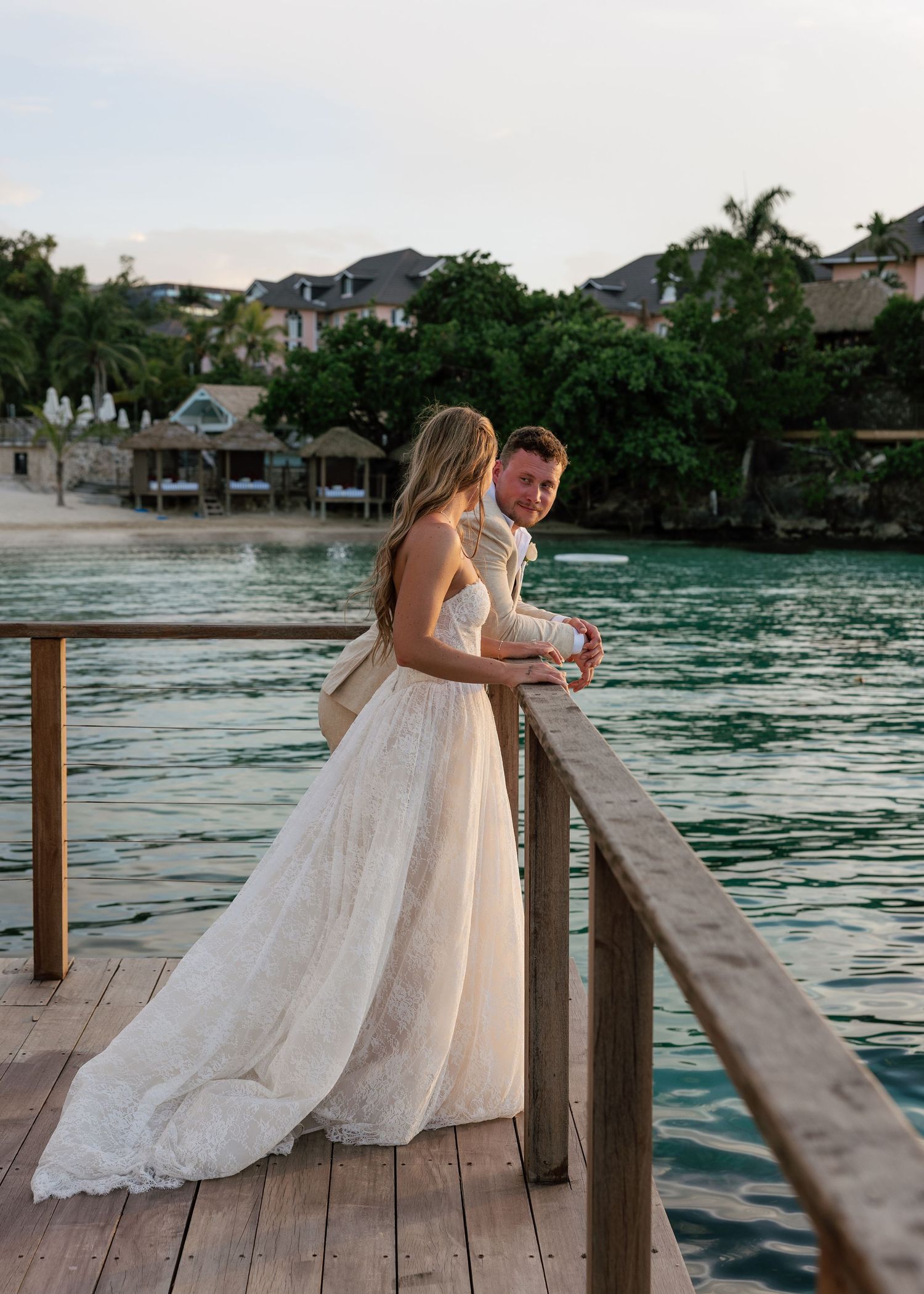 Bride and groom share a romantic moment on a wooden dock overlooking turquoise waters at a tropical resort.