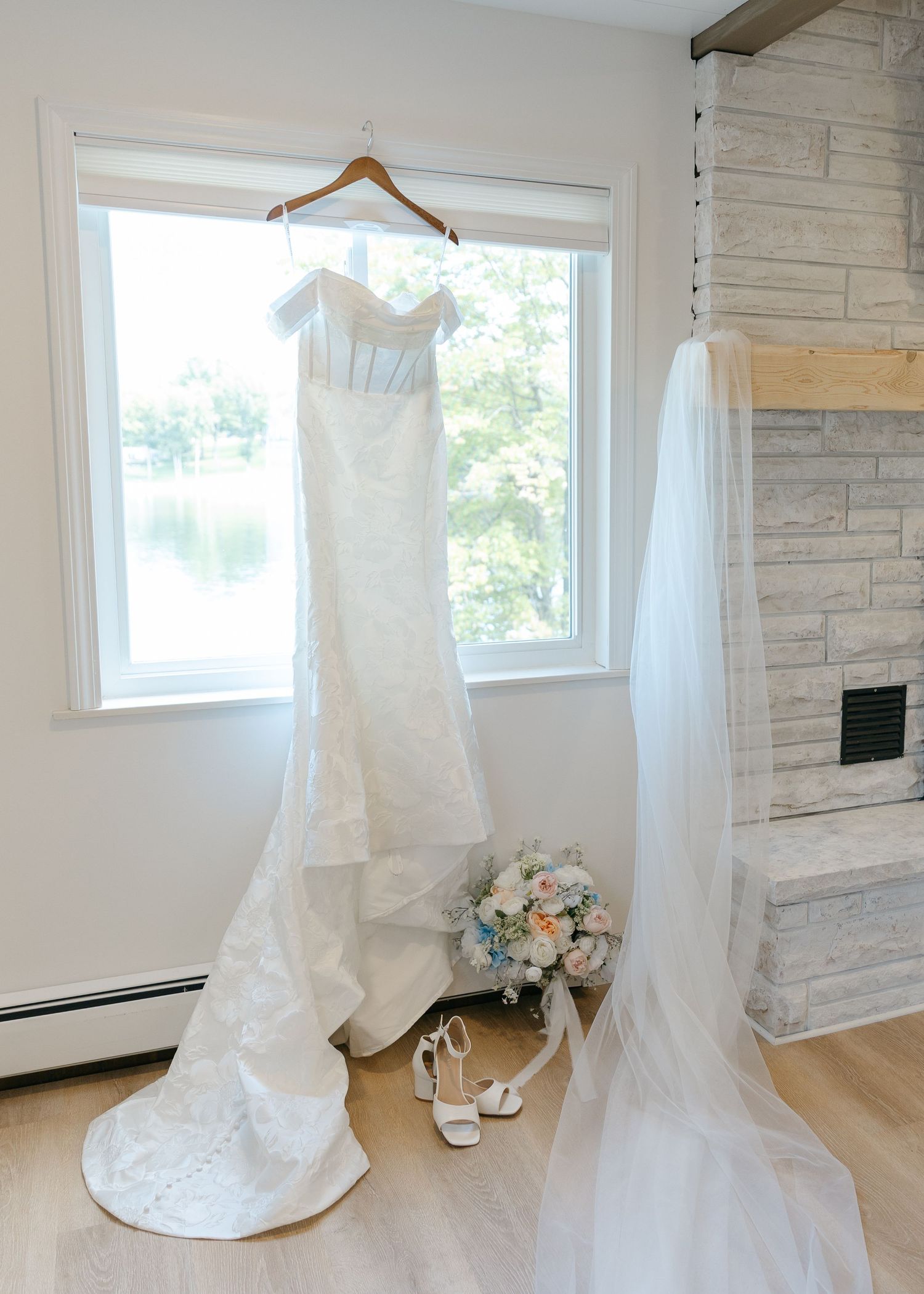 Wedding dresses hanging in bright room with stone accent wall and windows.