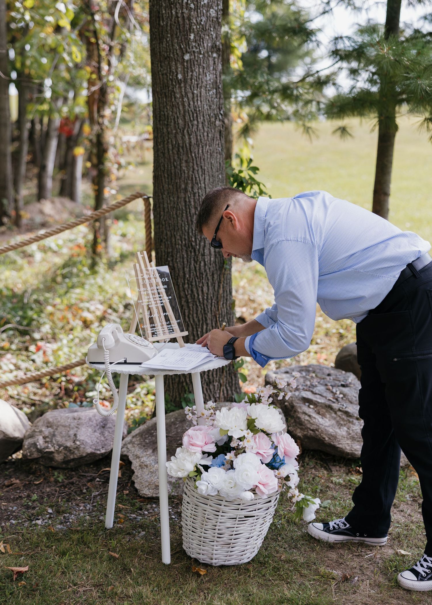 Wedding decor and floral arrangements being set up in outdoor woodland setting.