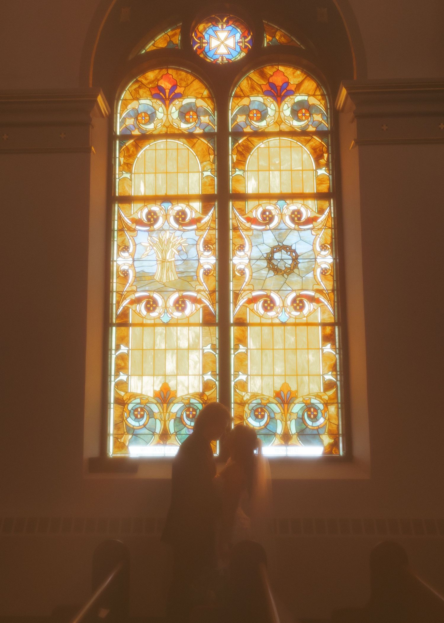 Silhouetted figures against beautiful stained glass church windows in warm lighting.
