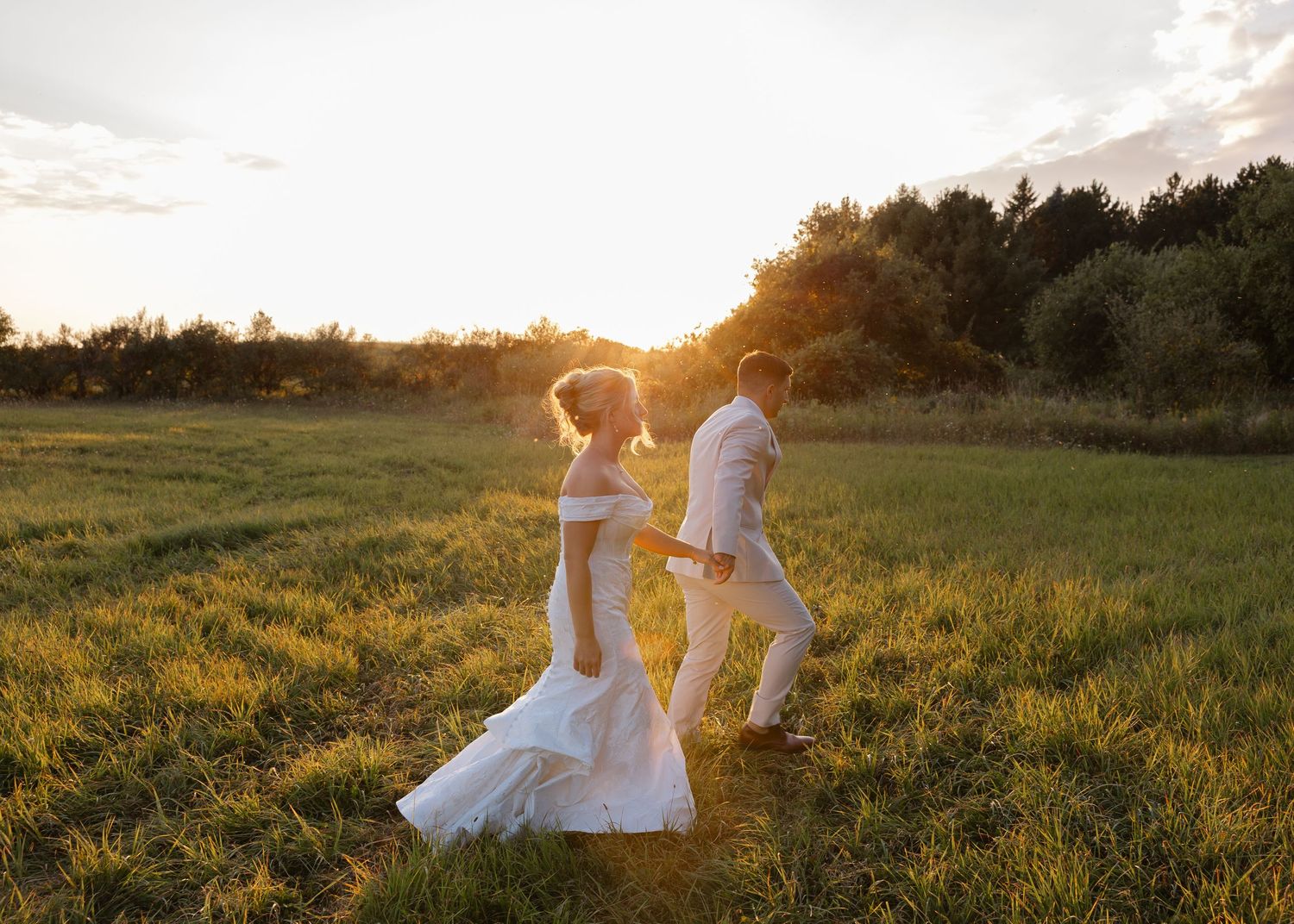 Wedding couple walking through sunlit field at golden hour.