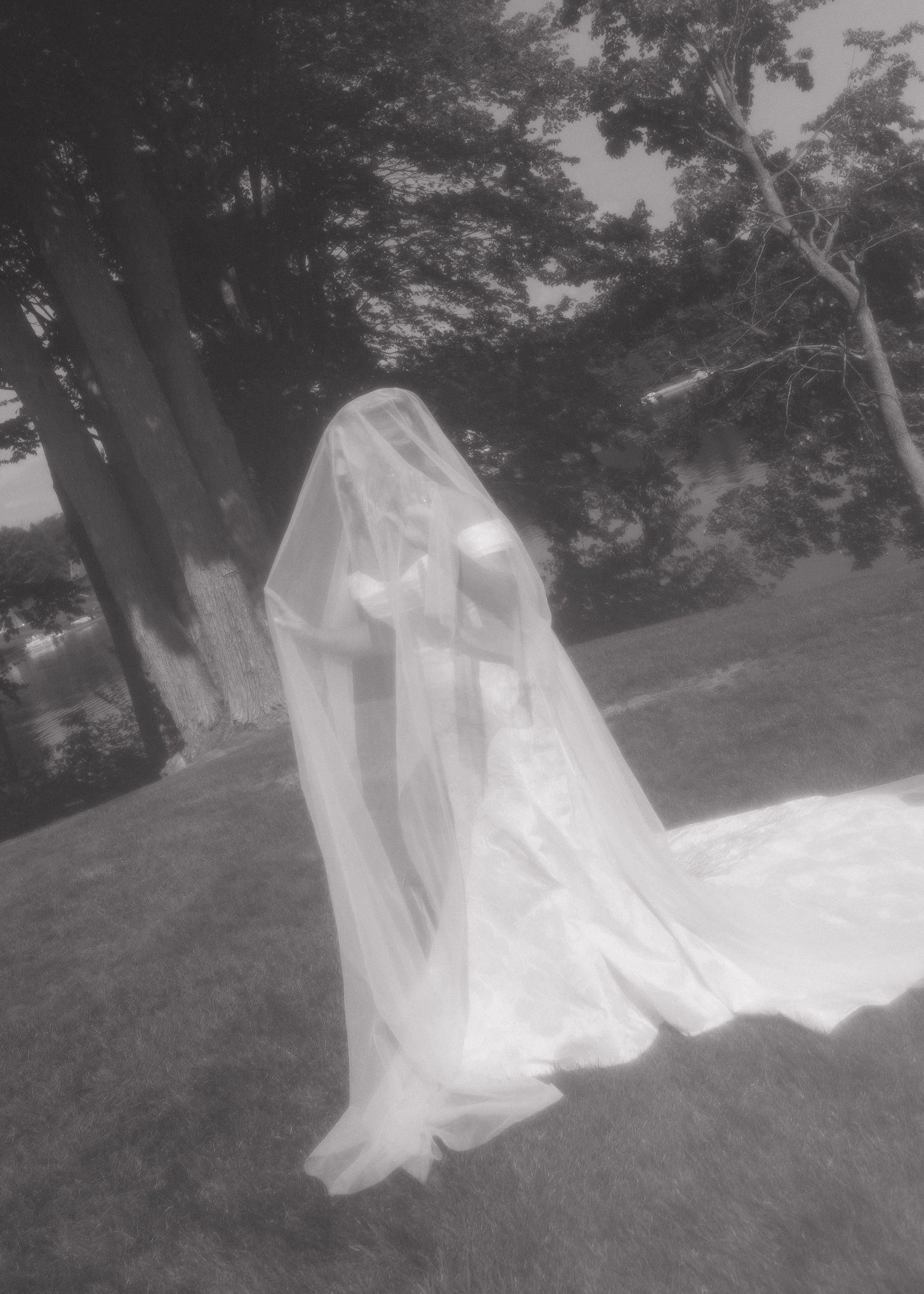 Ethereal black and white photo of flowing wedding dress and veil in natural outdoor setting.