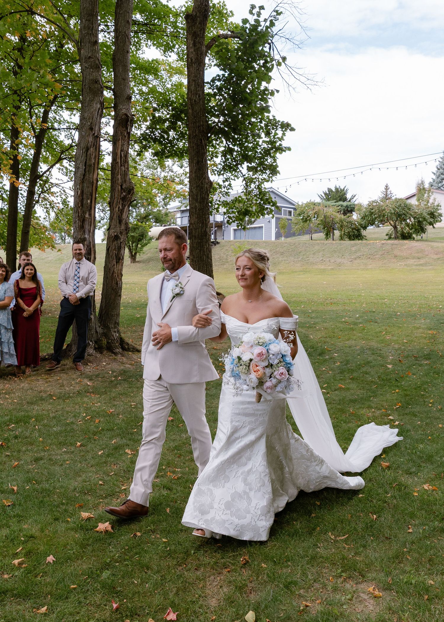 Wedding party members dance and celebrate on a grassy lawn during an outdoor reception.