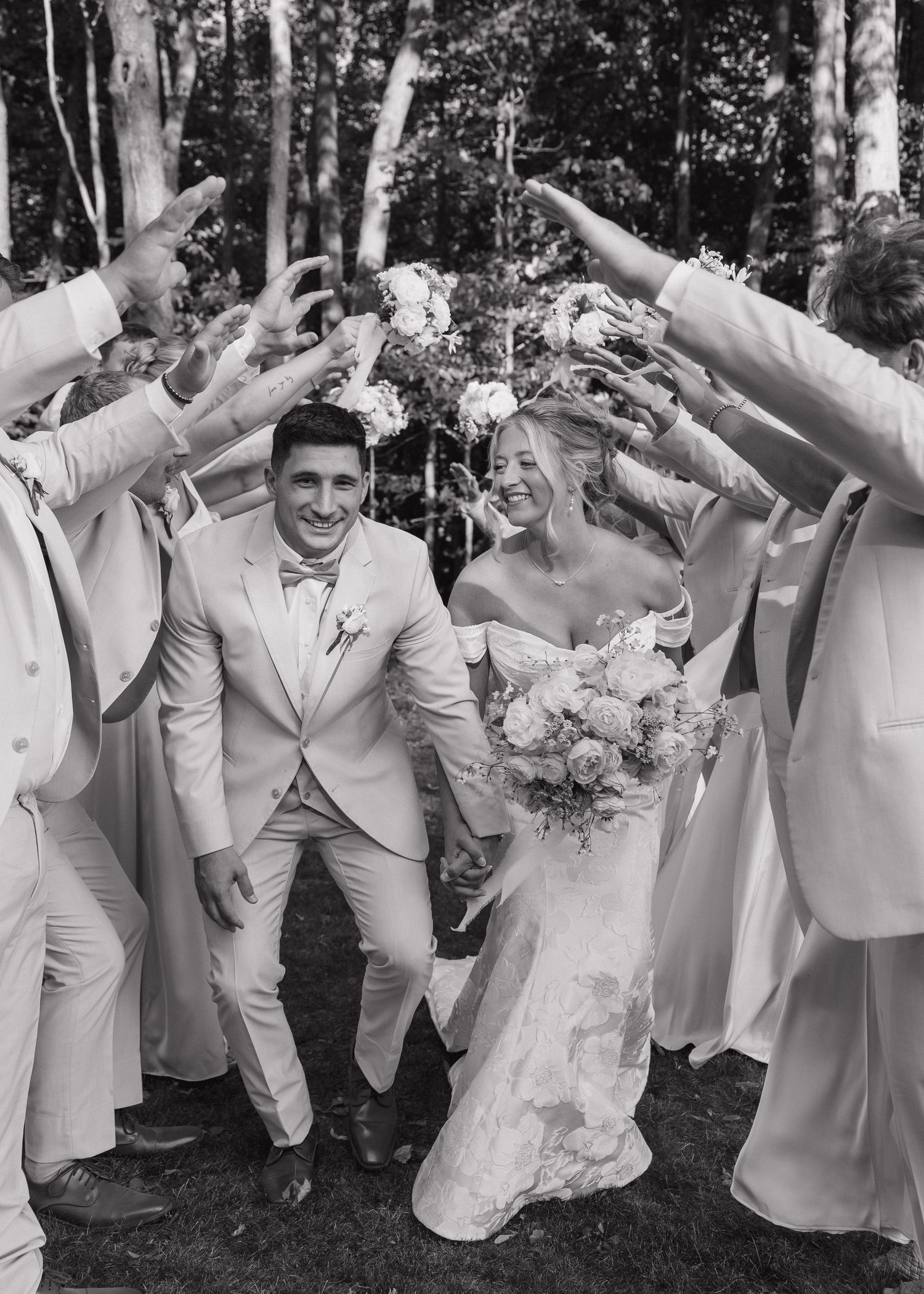 Wedding party in light colored suits poses playfully in a line outdoors.