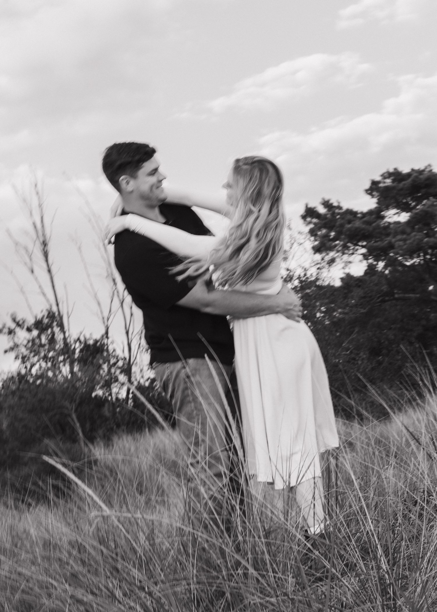 A black and white romantic portrait of a couple embracing in a field.