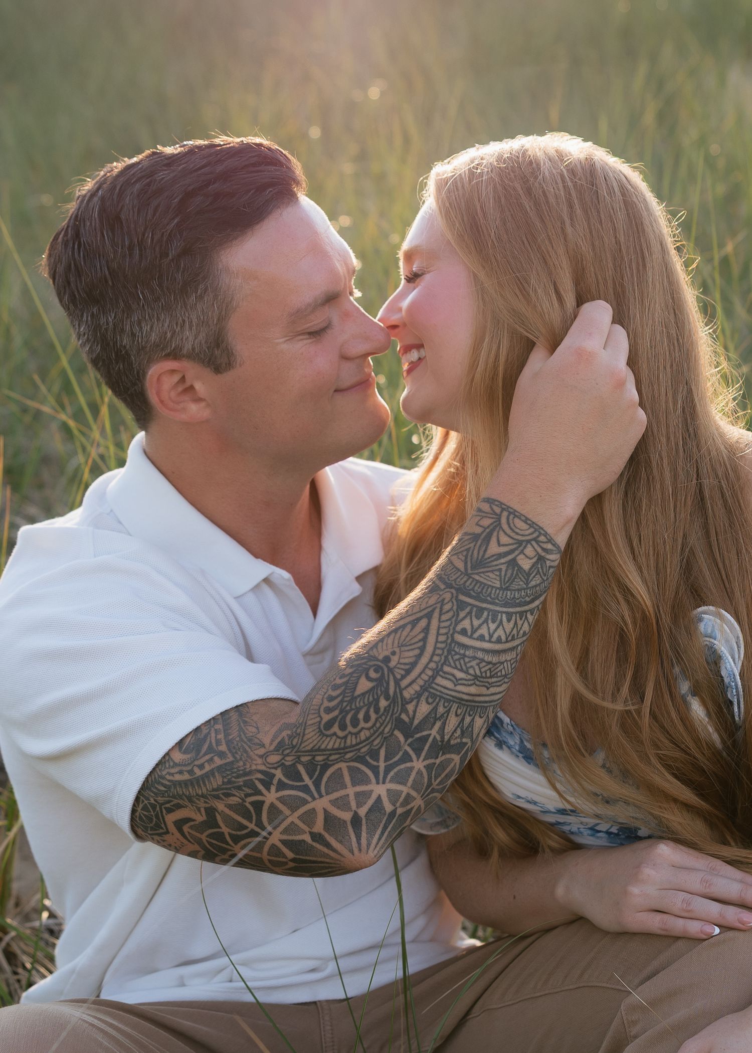Couple sharing a romantic moment outdoors in a field, man with sleeve tattoo gently holding woman's face.