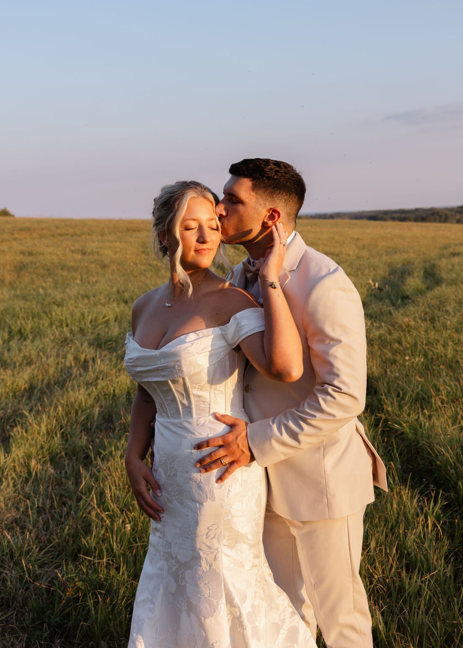Romantic sunset photoshoot of newlyweds embracing in a golden field.