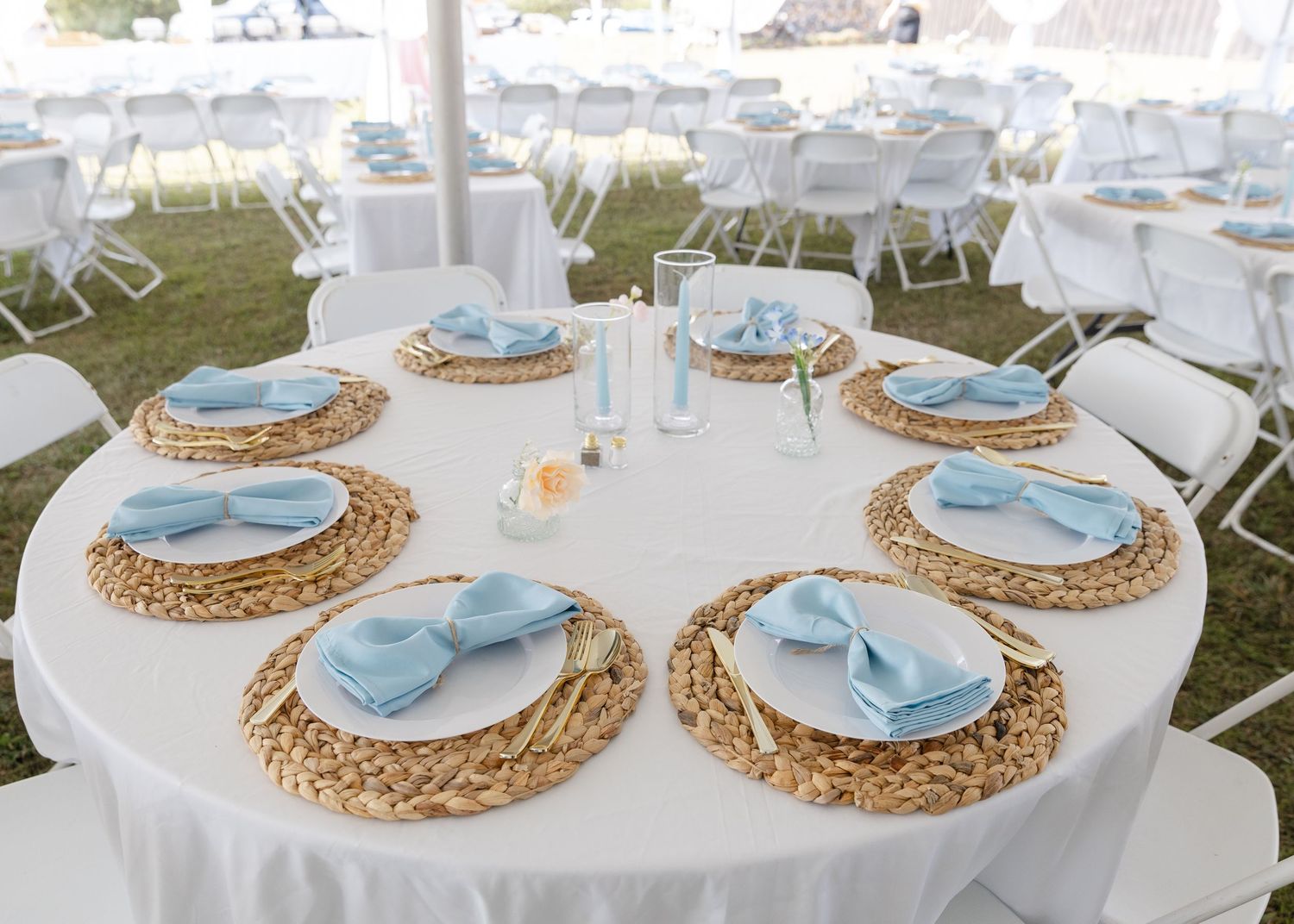 Table settings with light blue plates on woven chargers at wedding reception.