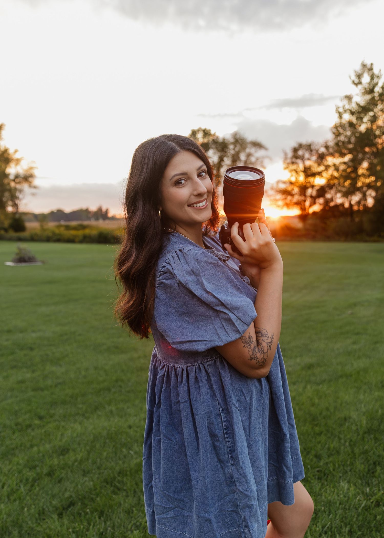 Person in denim dress holding coffee cup during golden hour in grassy field.