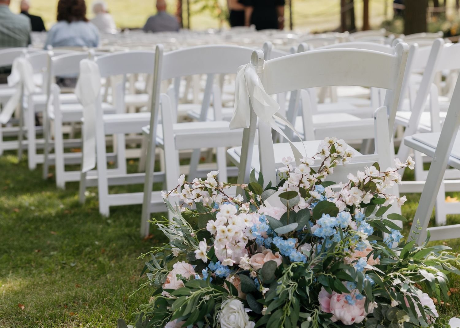 White wedding ceremony chairs arranged outdoors with floral decorations.