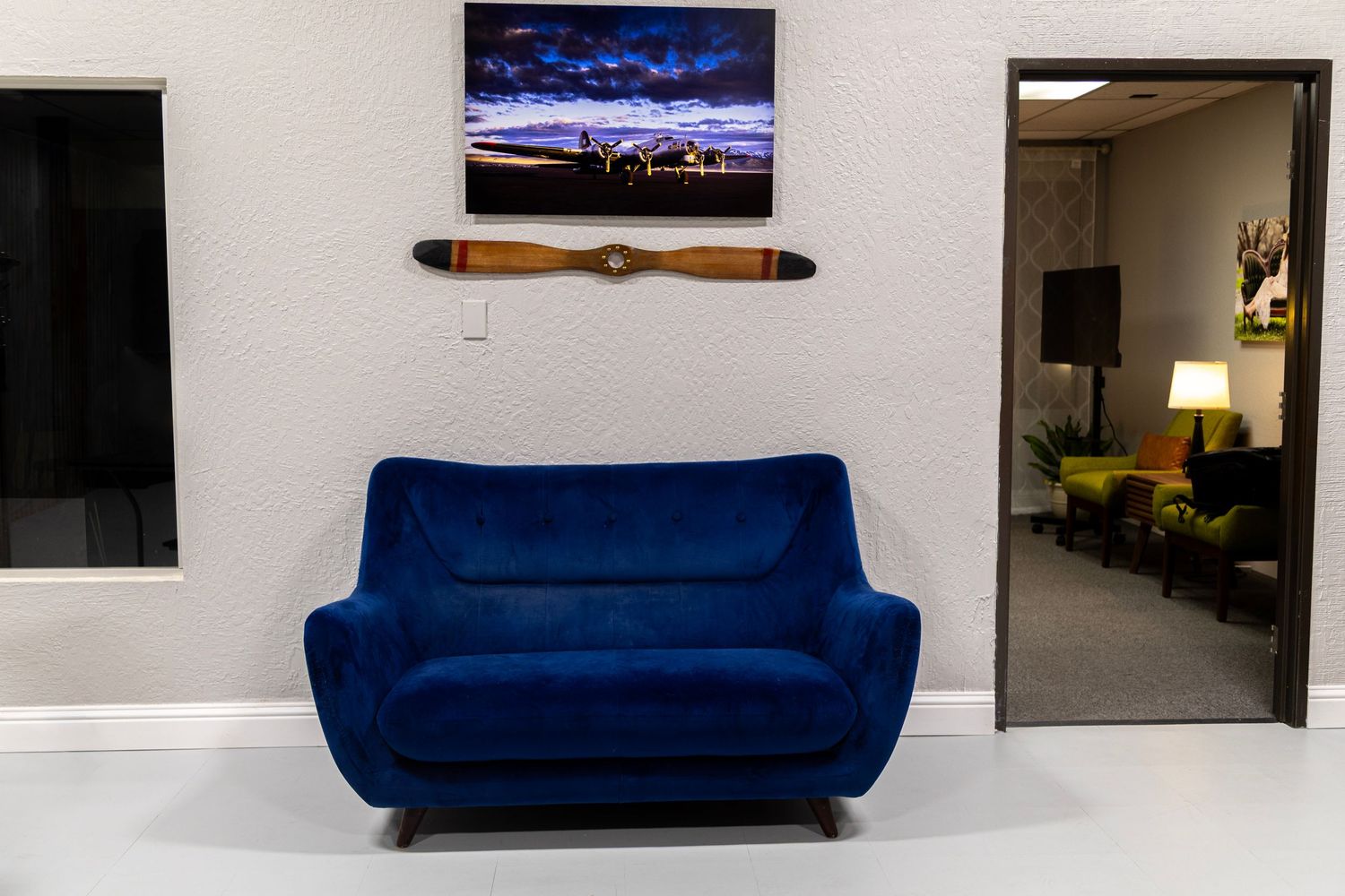 Blue velvet loveseat sofa in a modern studio space with vintage propeller wall decor and framed landscape artwork.