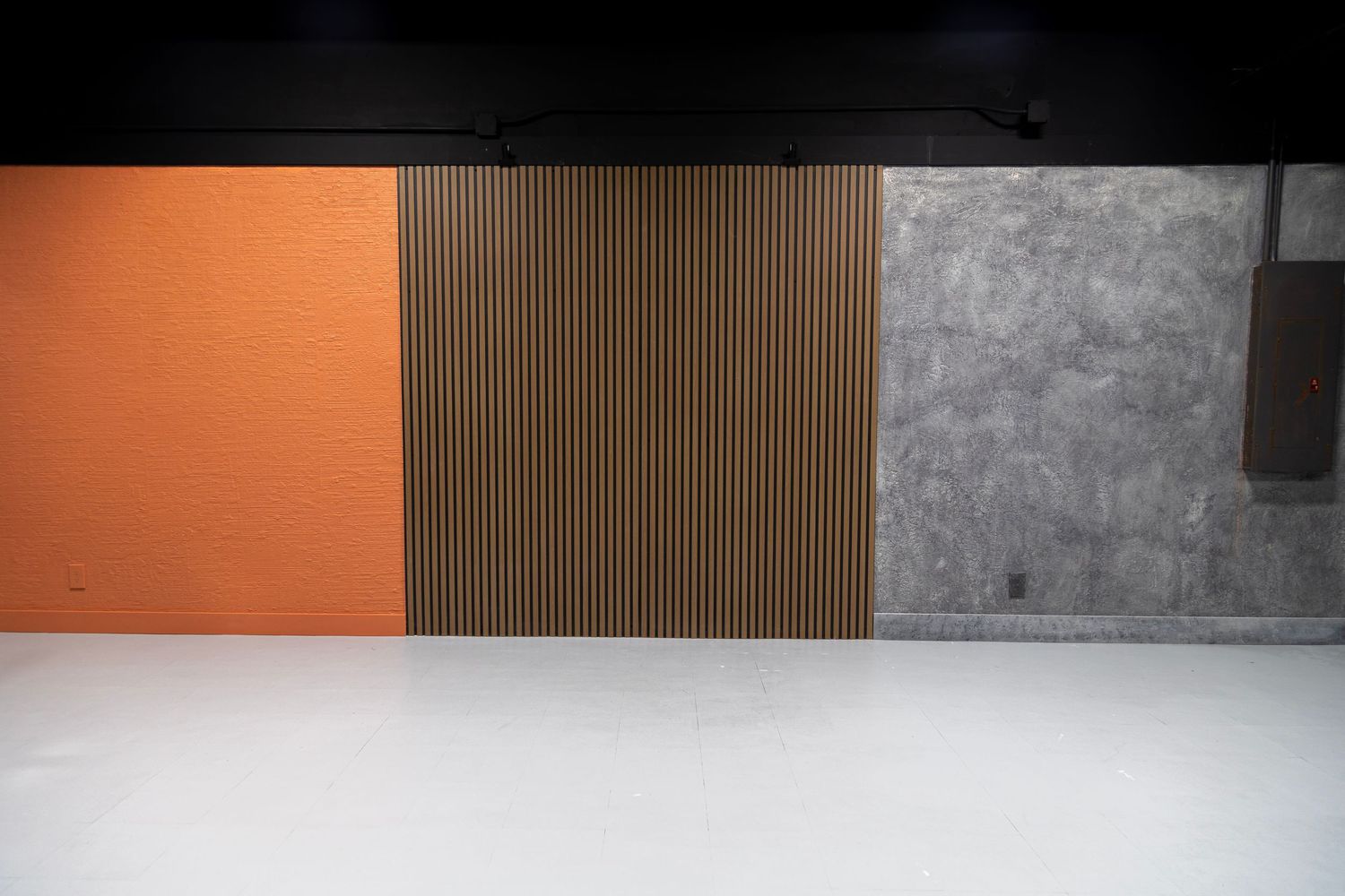 Modern studio backdrop wall featuring orange textured, warm wood slat, and gray concrete panel sections.
