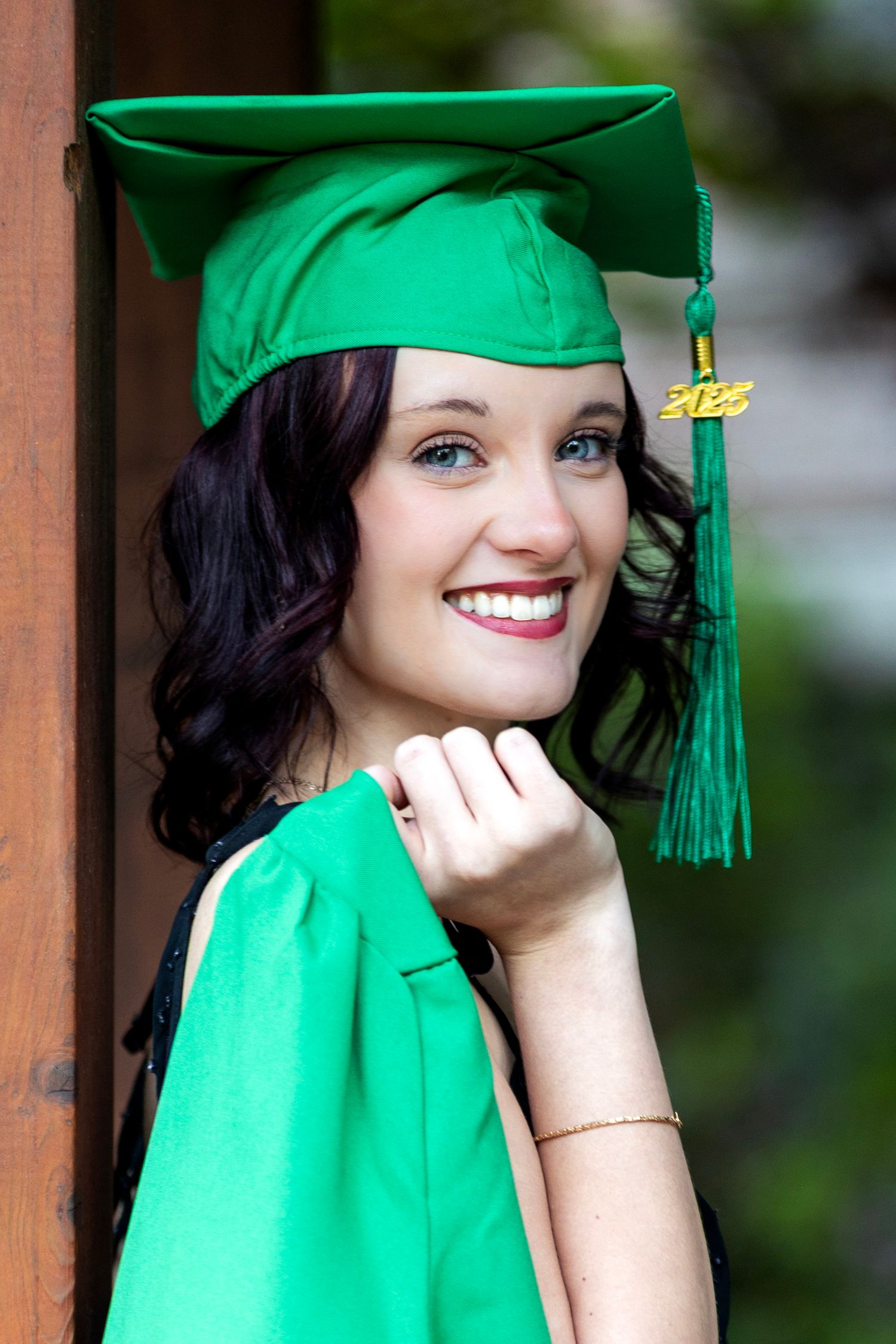 Smiling graduate in green cap and gown poses outdoors celebrating class of 2023.