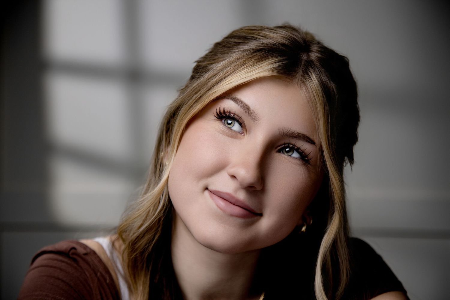 Young blonde woman with blue eyes smiling softly in a portrait with dramatic light and shadow background.