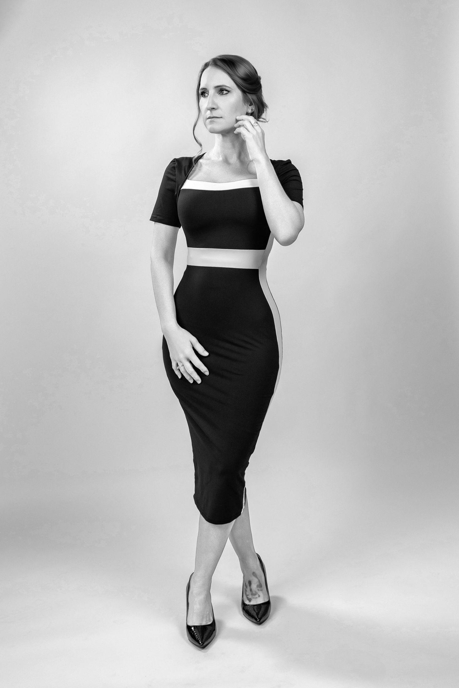 Black and white photo of a woman in a two-piece black outfit with crop top and pencil skirt, posing in heels.