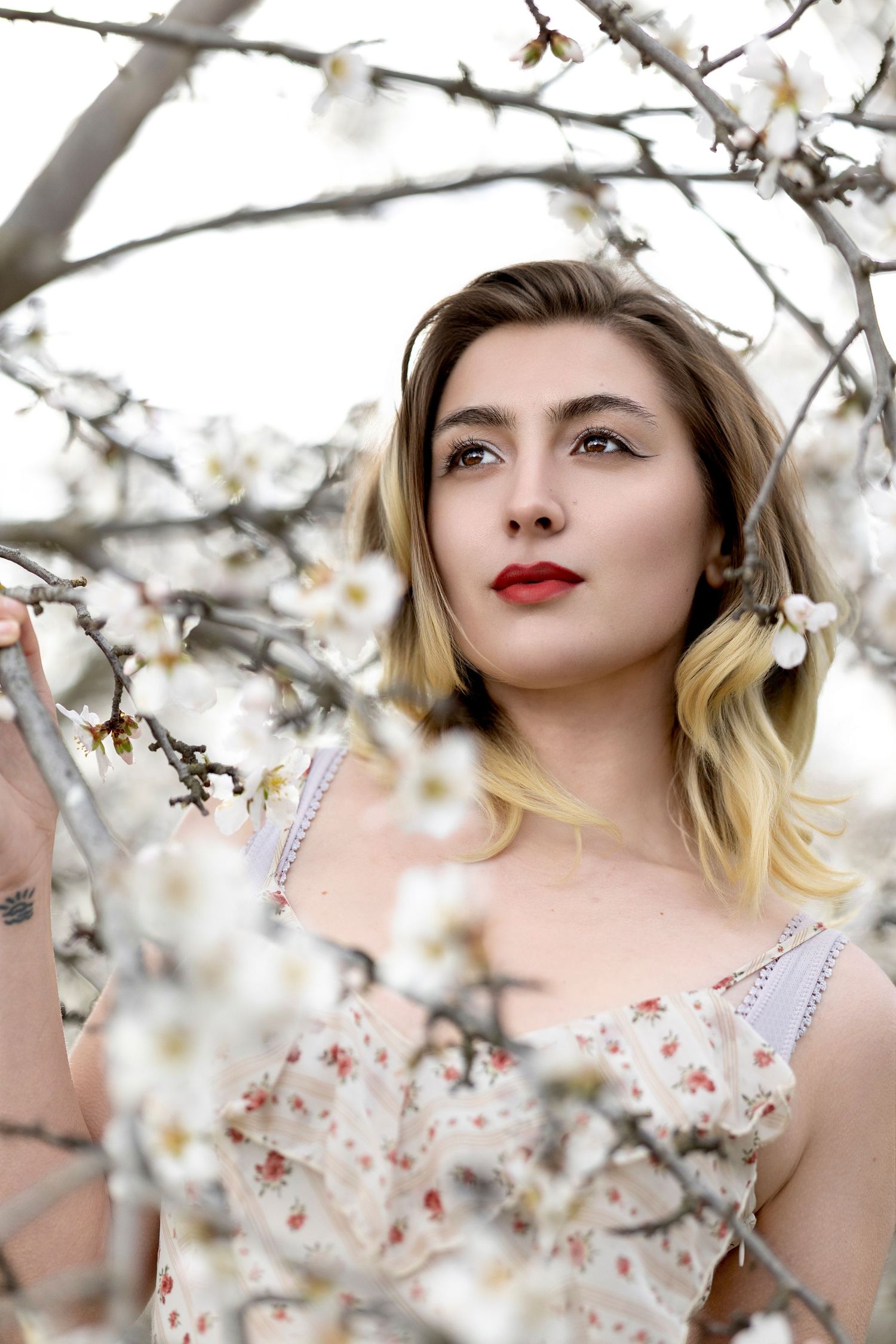 Young blonde woman with red lips surrounded by white almond blossoms in spring.