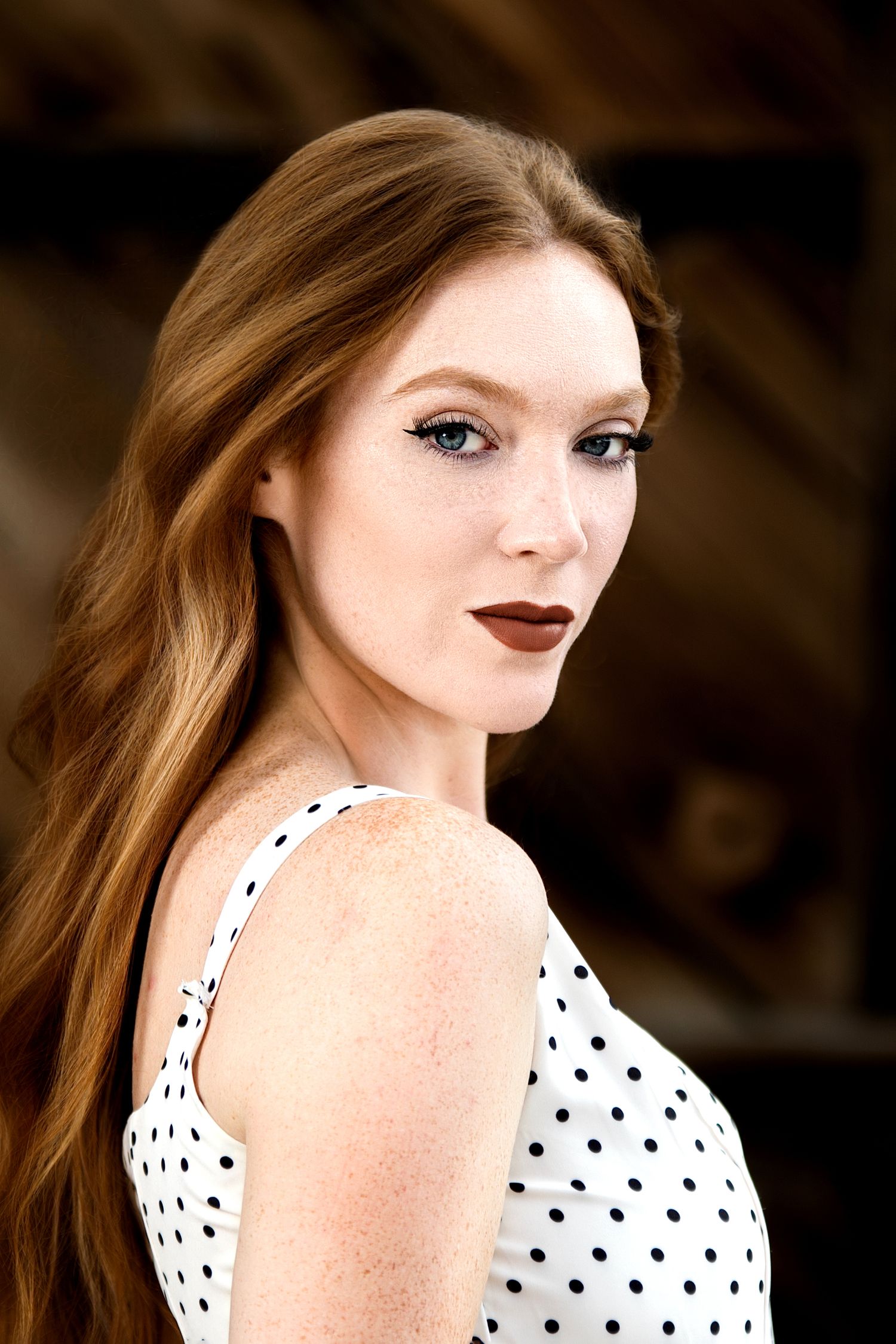Redhead woman with freckles wearing a white polka dot dress poses for a portrait photo.