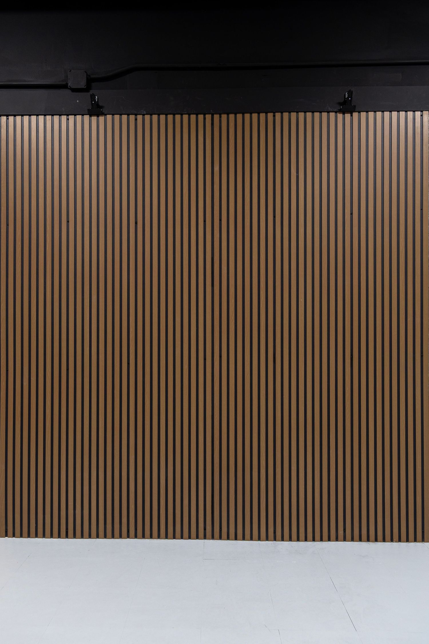 Warm brown vertical wood slat panel backdrop wall in a modern photography studio with black ceiling.