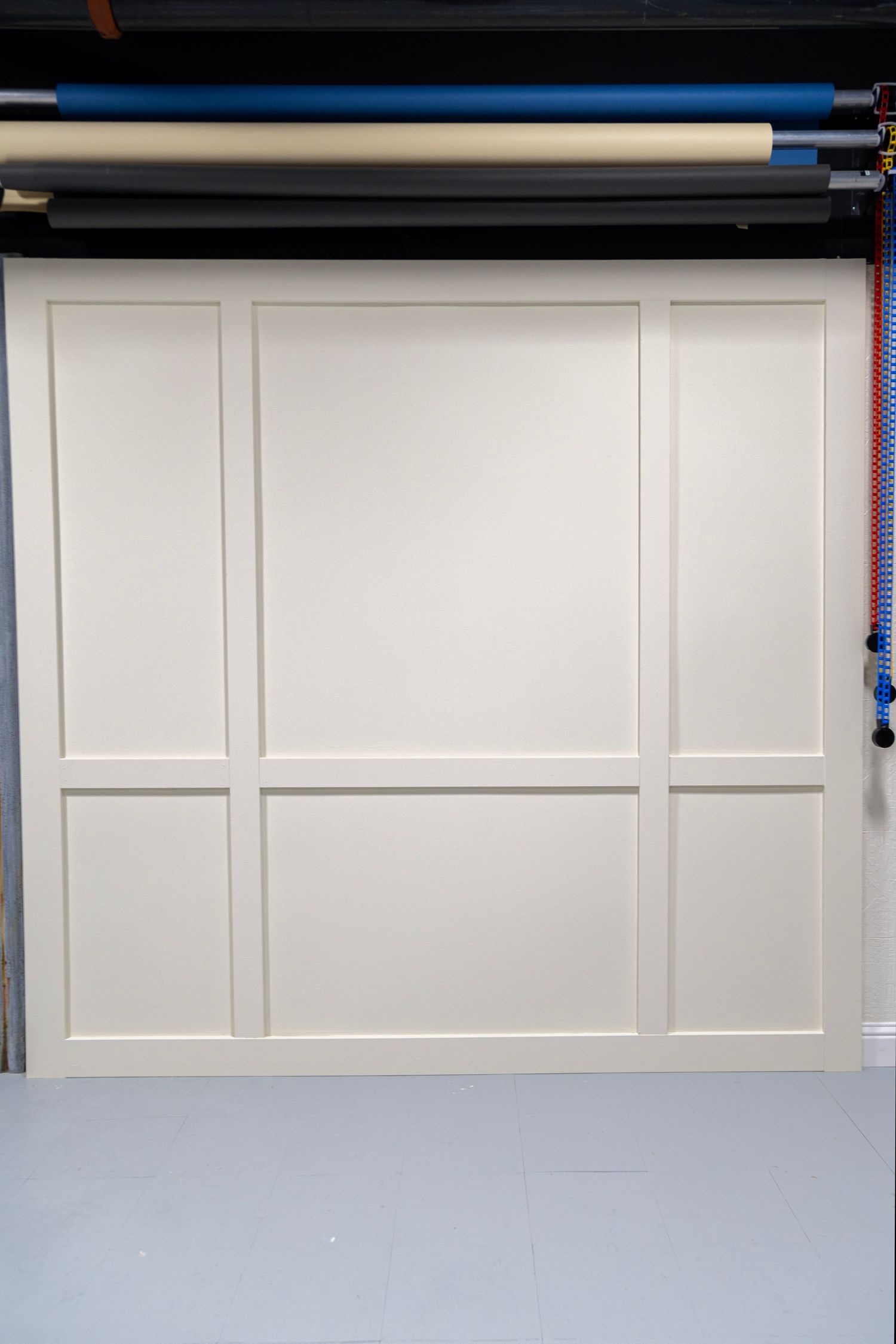 Clean white wainscoting panel backdrop wall in a photography studio with colorful backdrop rolls overhead.