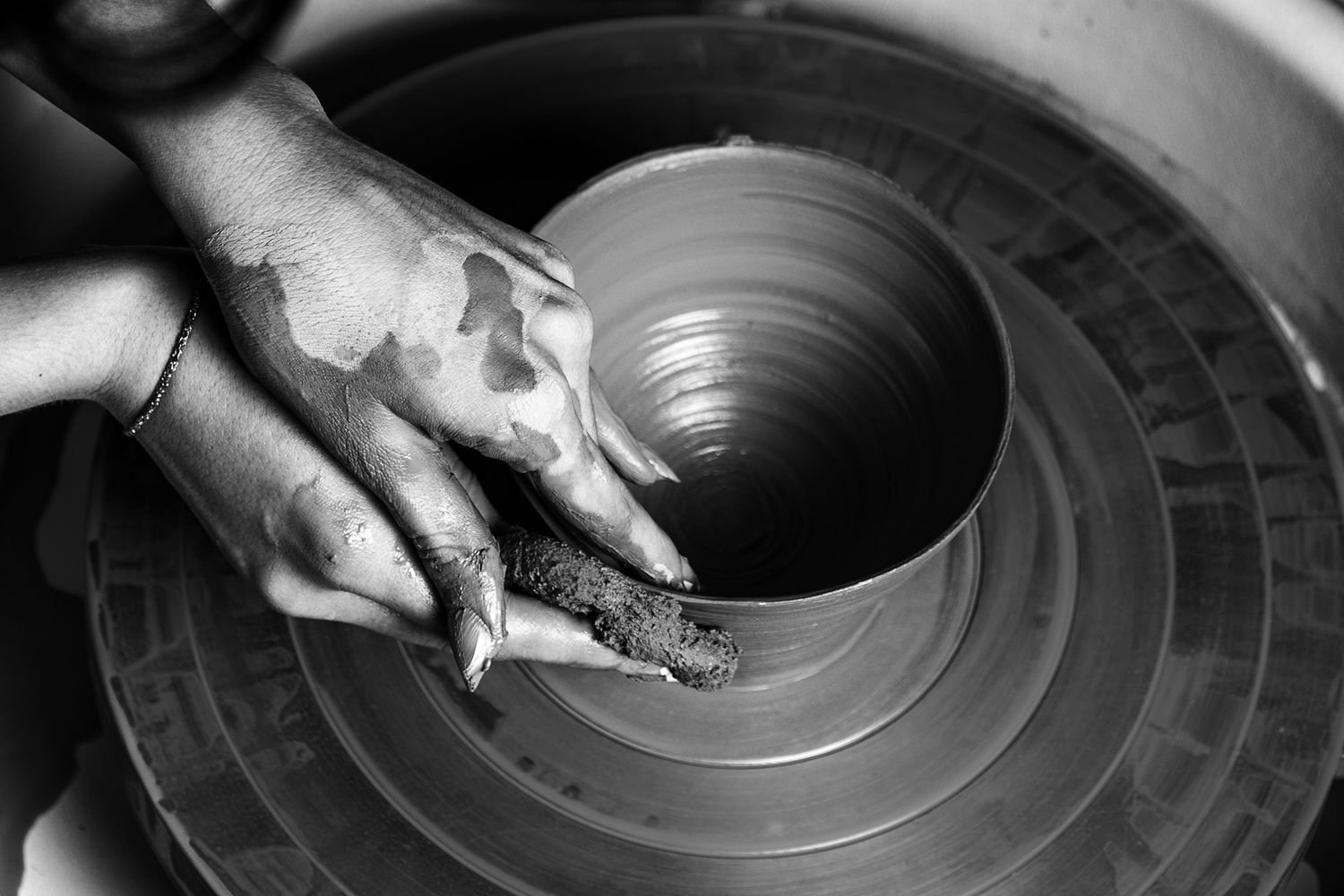 Black and white close-up of hands shaping clay on a pottery wheel.